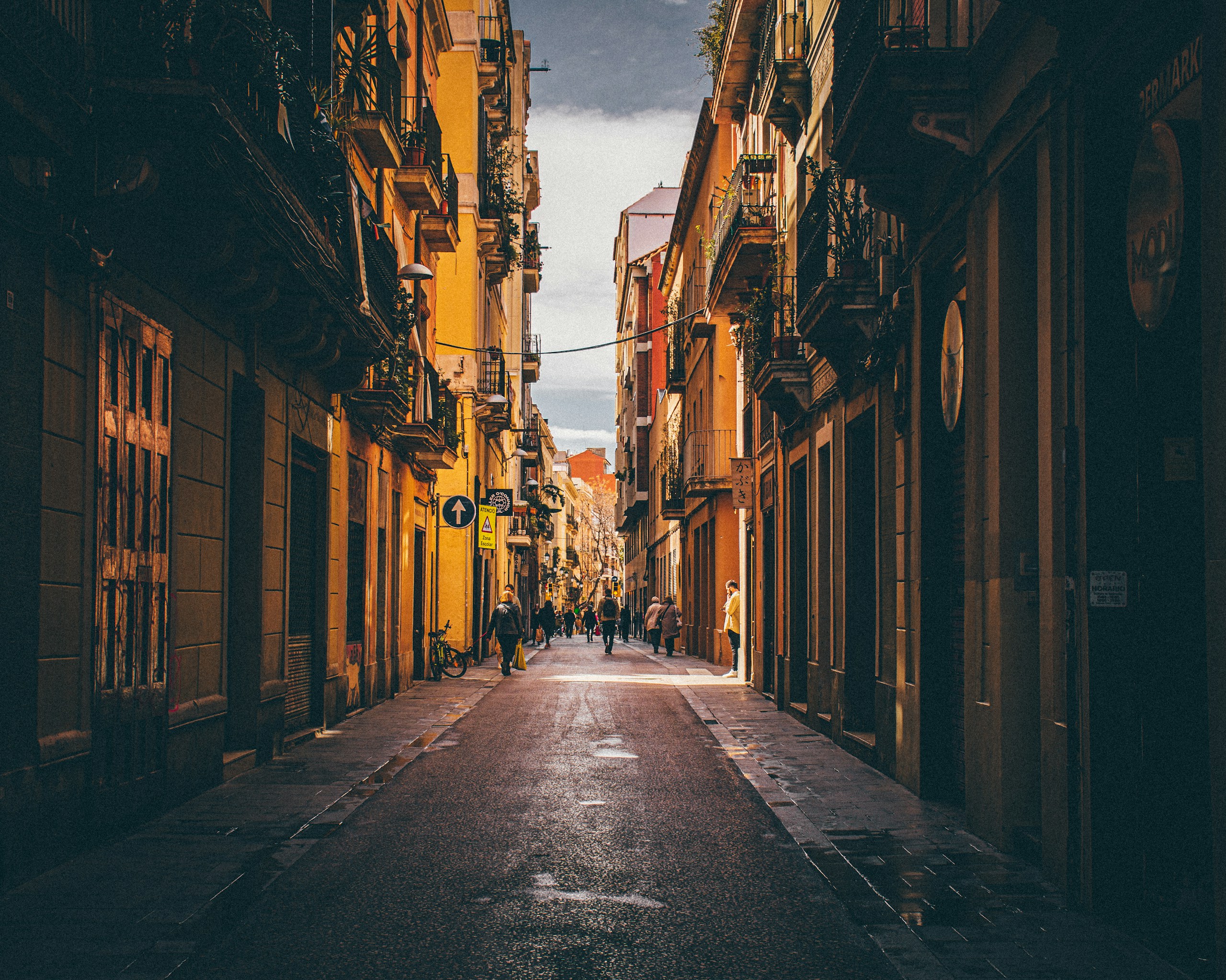 Narrow city street lined with tall buildings HD Wallpaper