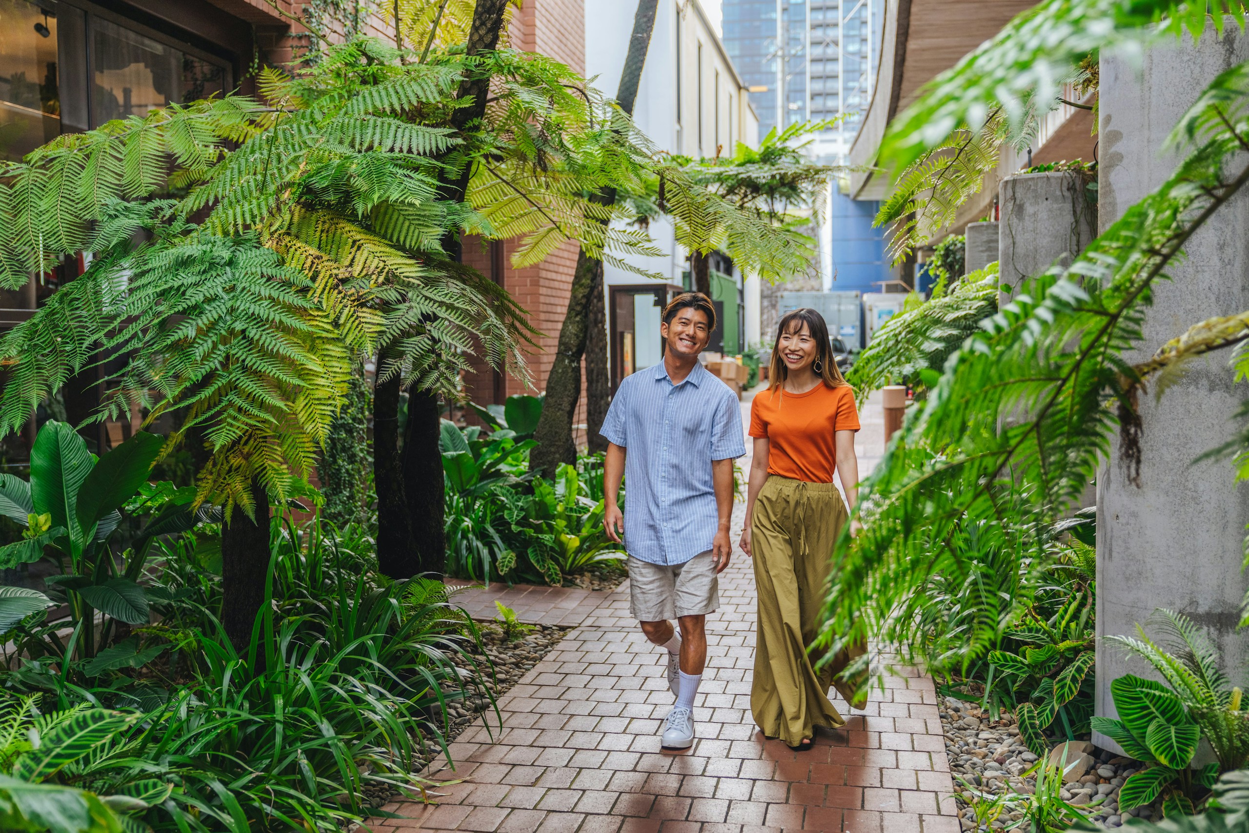 Couple walking through a lush urban garden path HD Wallpaper