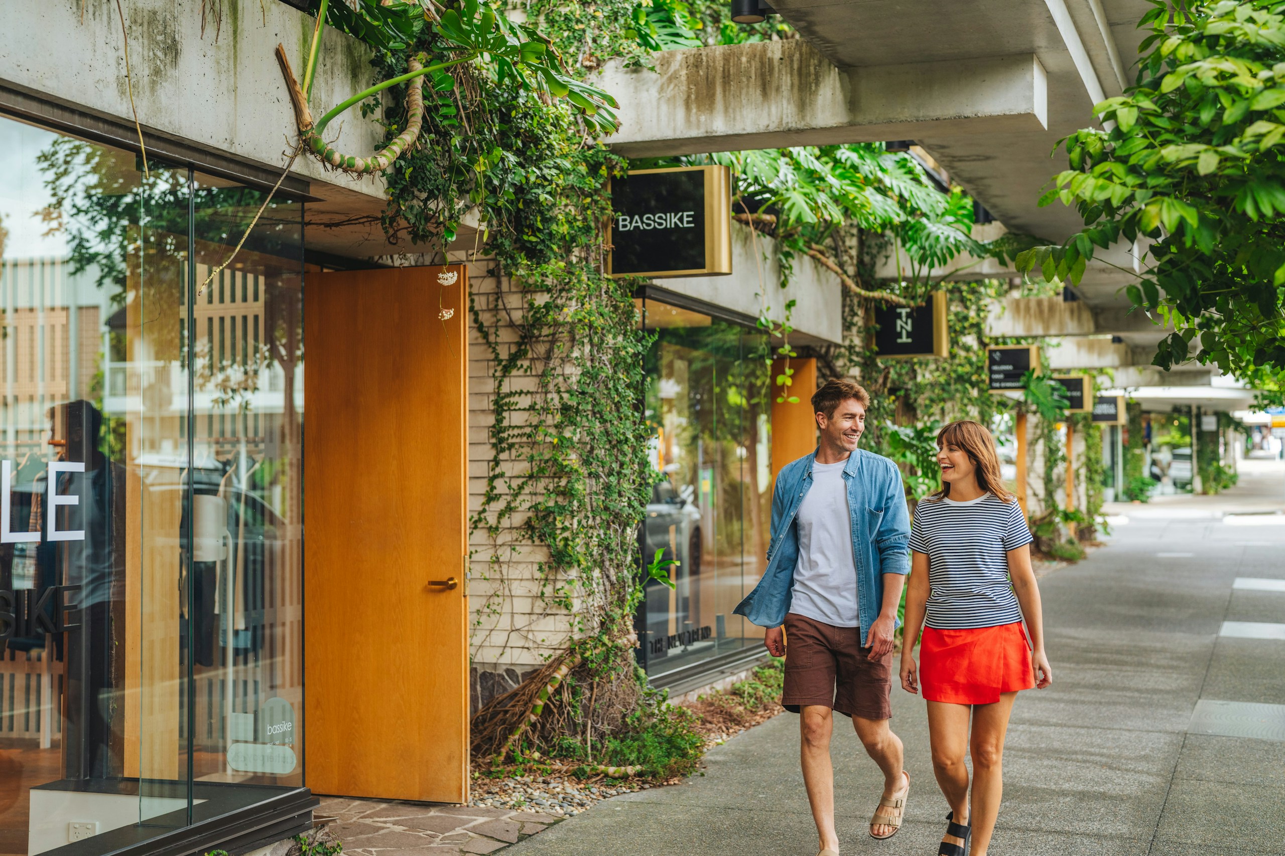 Couple walking past shops with lush greenery HD Wallpaper
