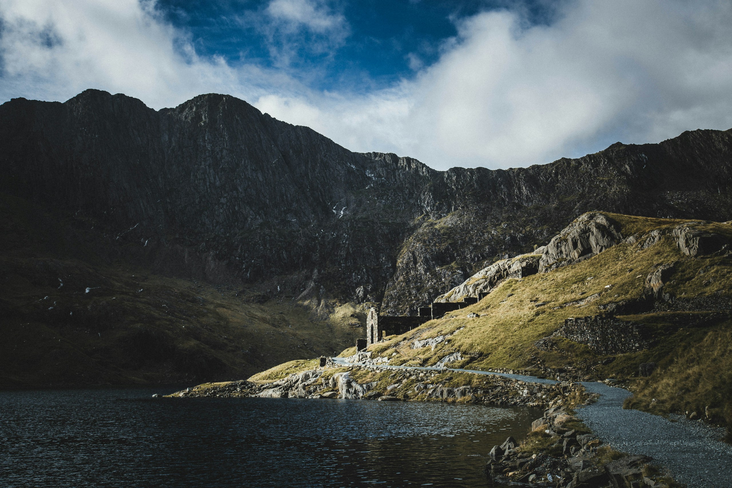 Ruined structure on a grassy mountainside by a lake HD Wallpaper