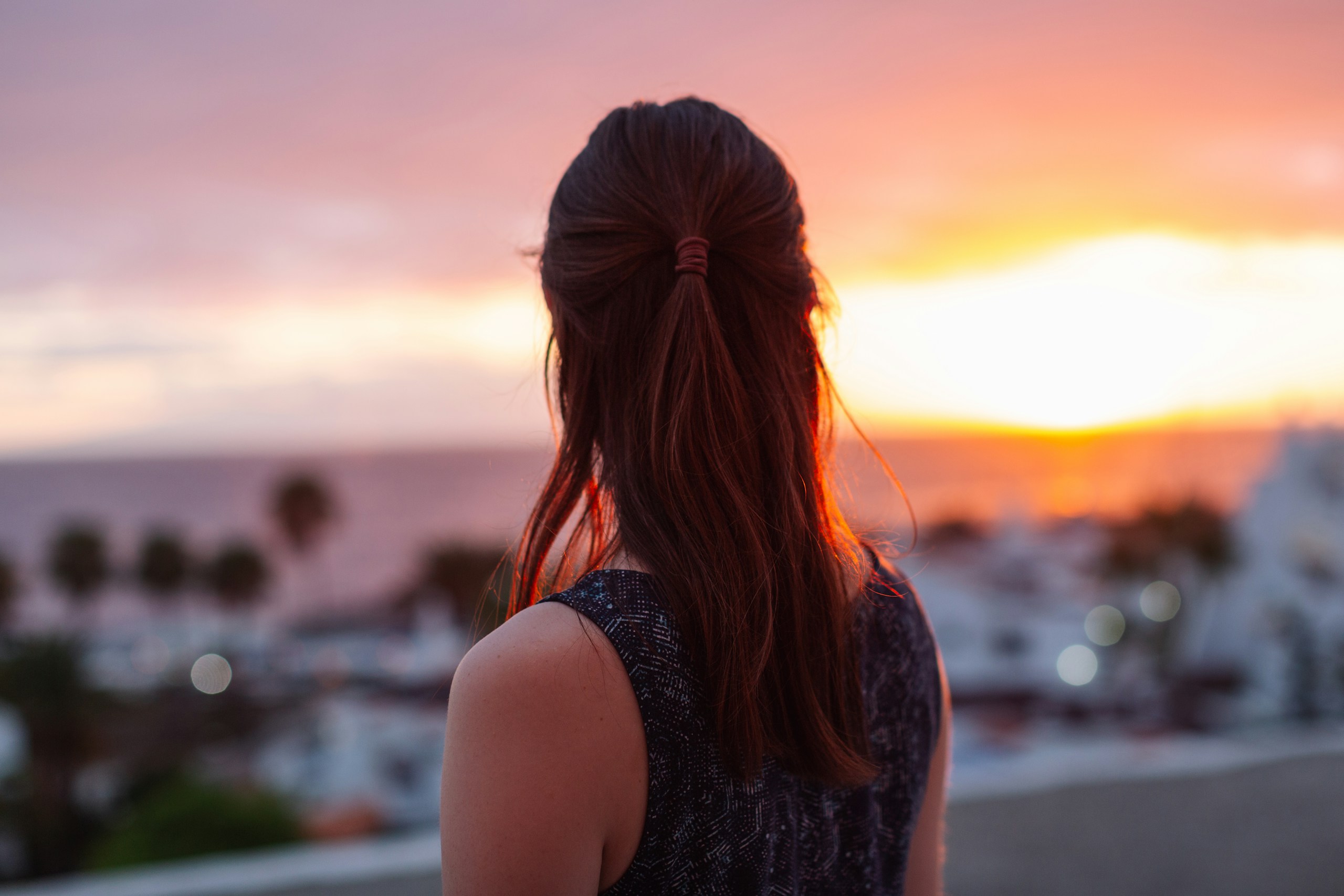 Woman watching a sunset over a coastal town HD Wallpaper