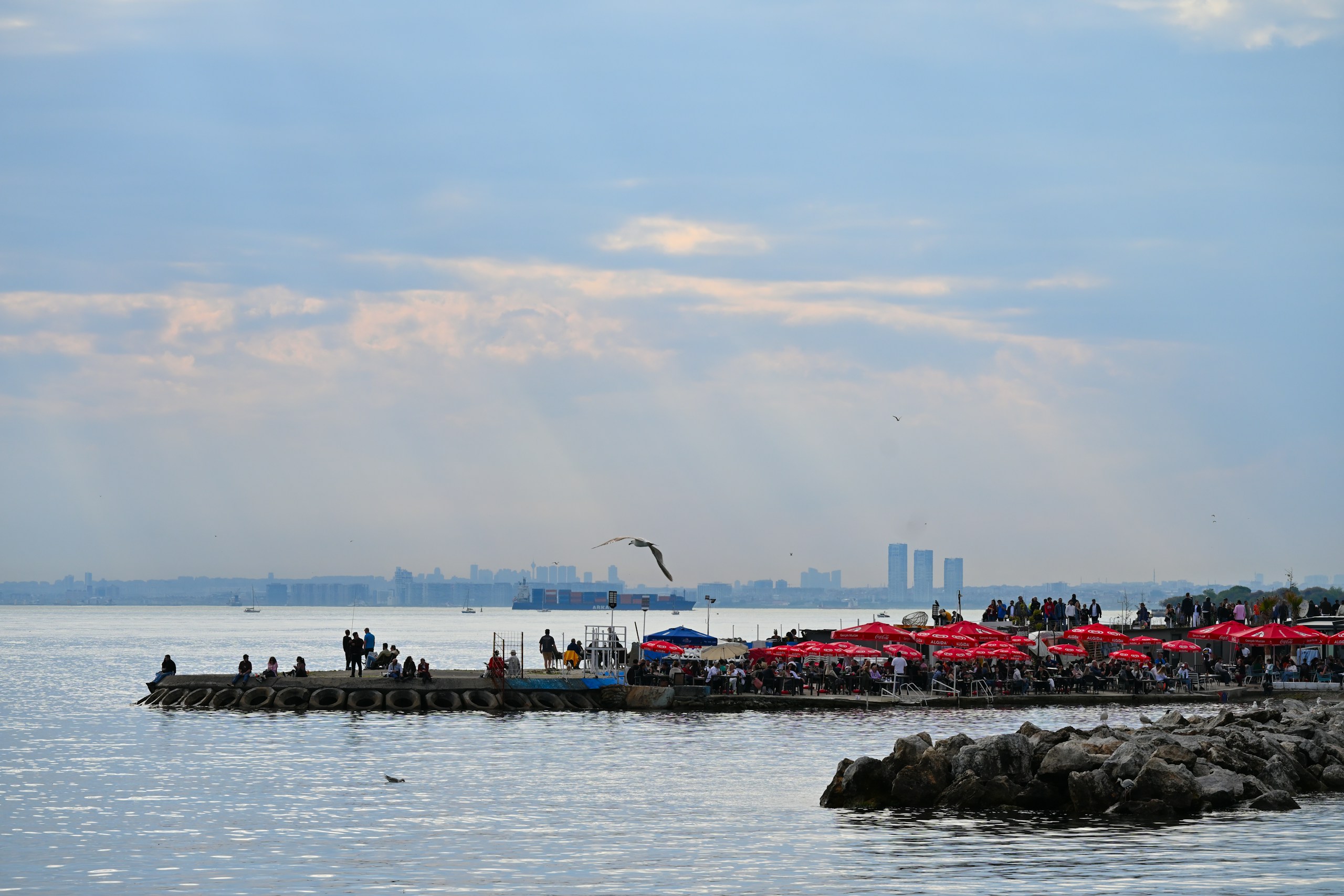 People enjoying a waterfront cafe with city skyline HD Wallpaper