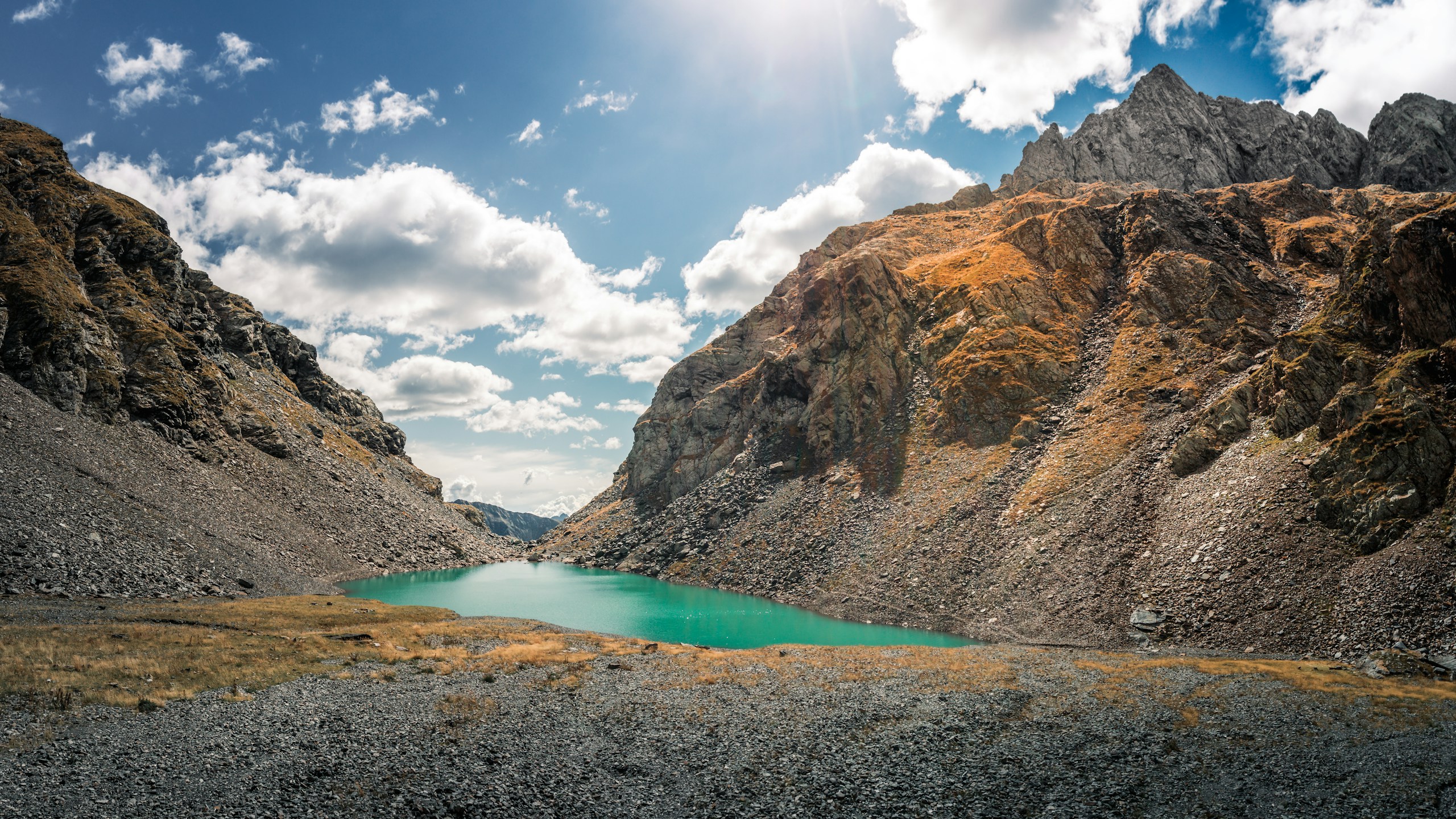 Turquoise lake nestled between rocky mountain slopes HD Wallpaper