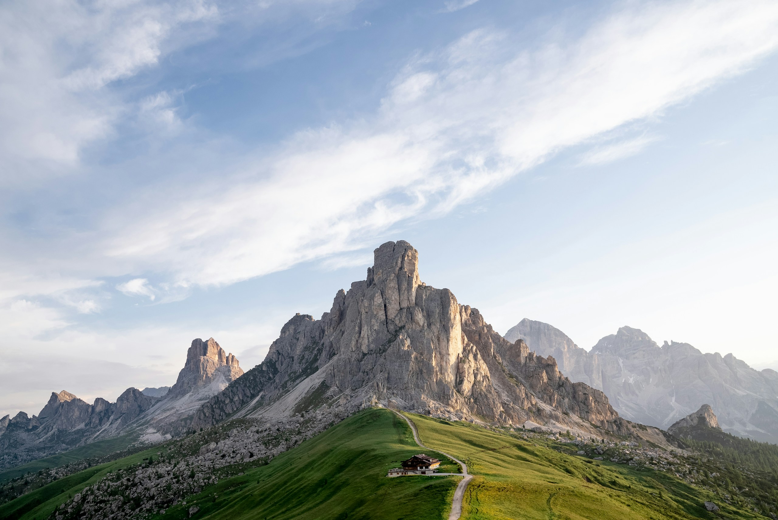 Mountain range with a small house on a grassy hill HD Wallpaper