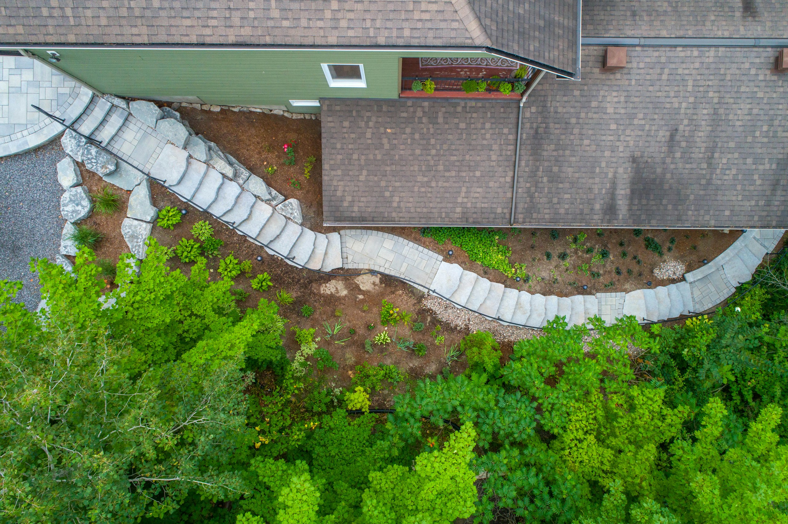 Aerial view of a house with a winding stone staircase and lush greenery HD Wallpaper