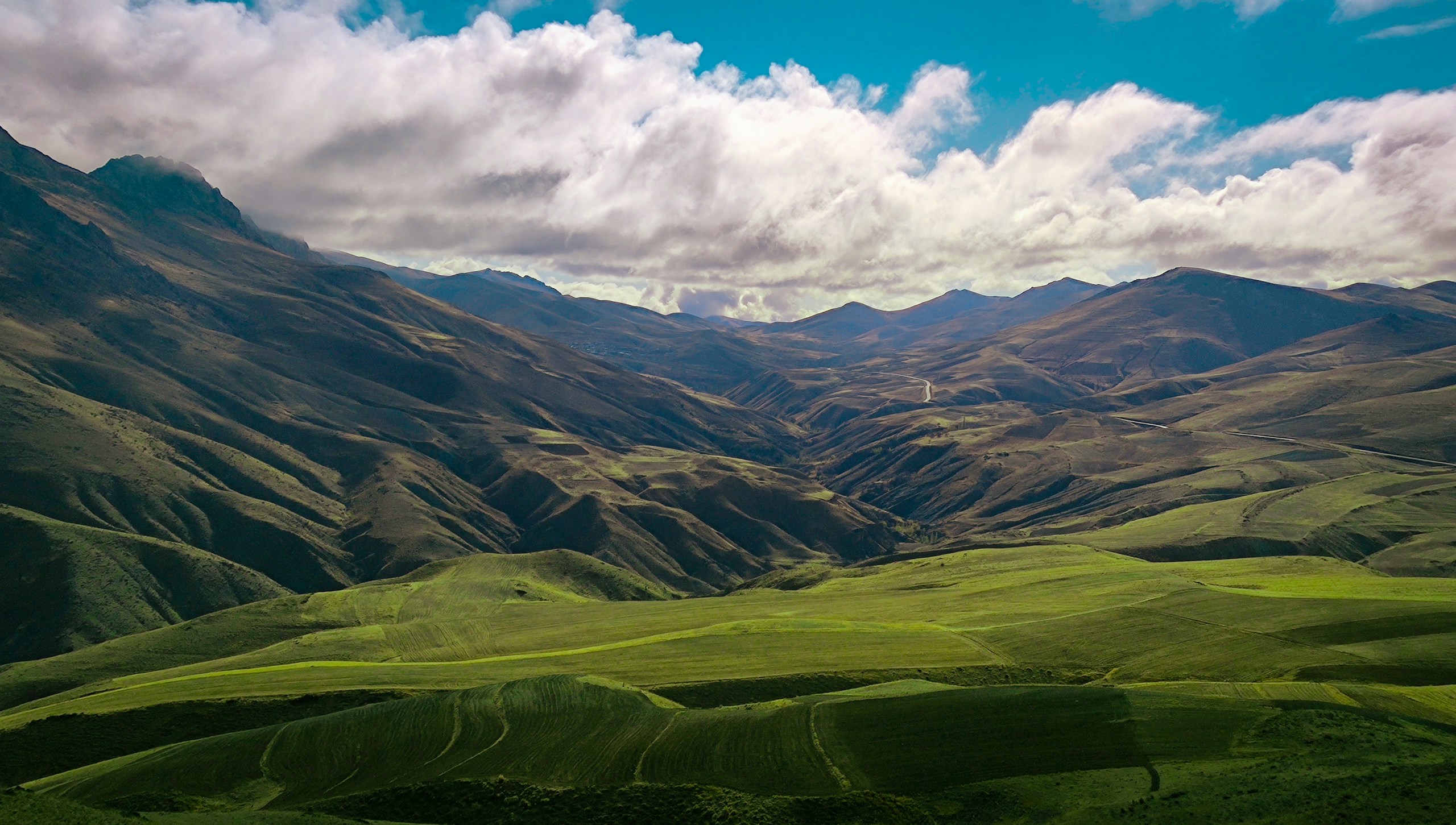 Rolling green hills and mountains under a cloudy sky HD Wallpaper