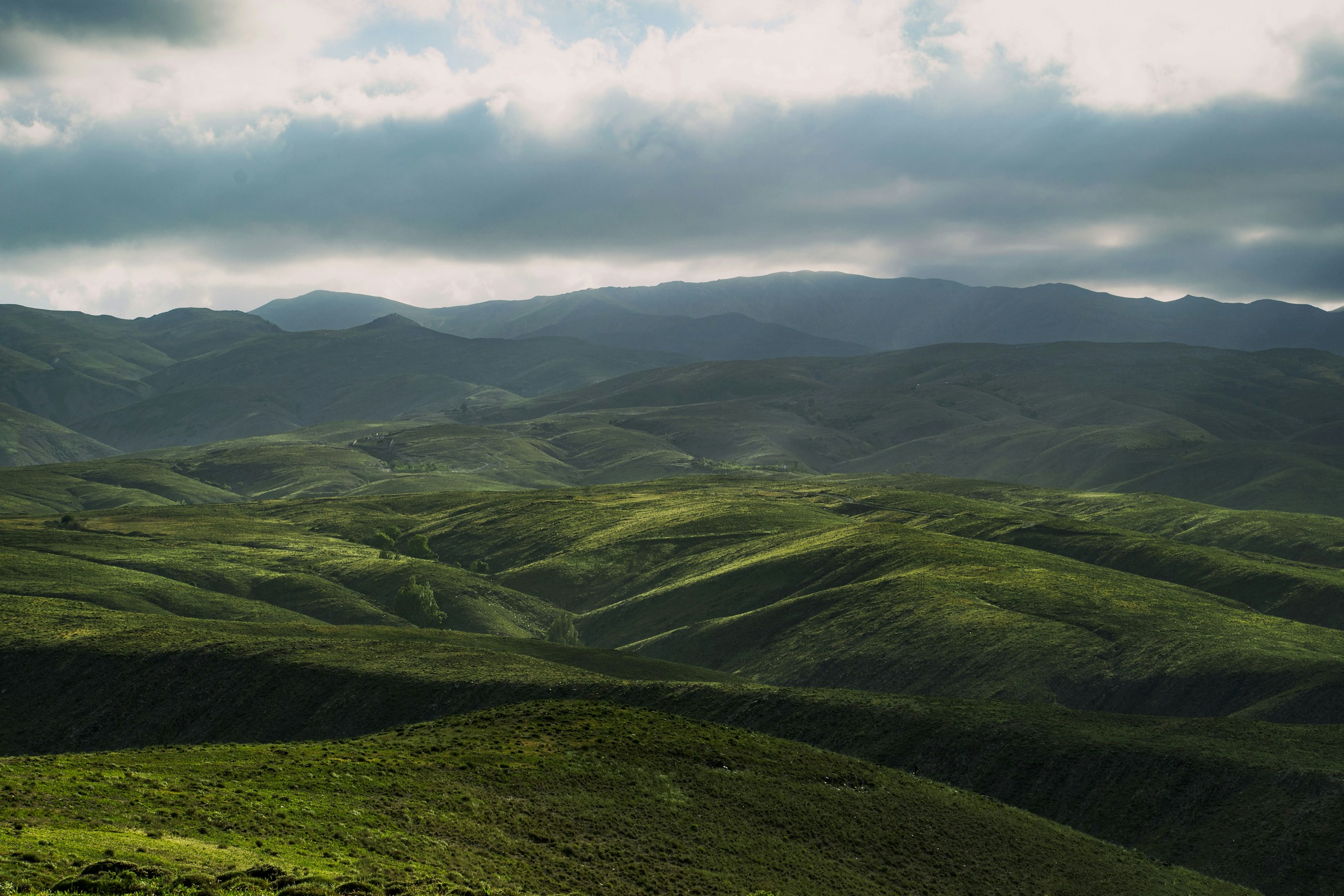 Rolling green hills under a cloudy sky HD Wallpaper