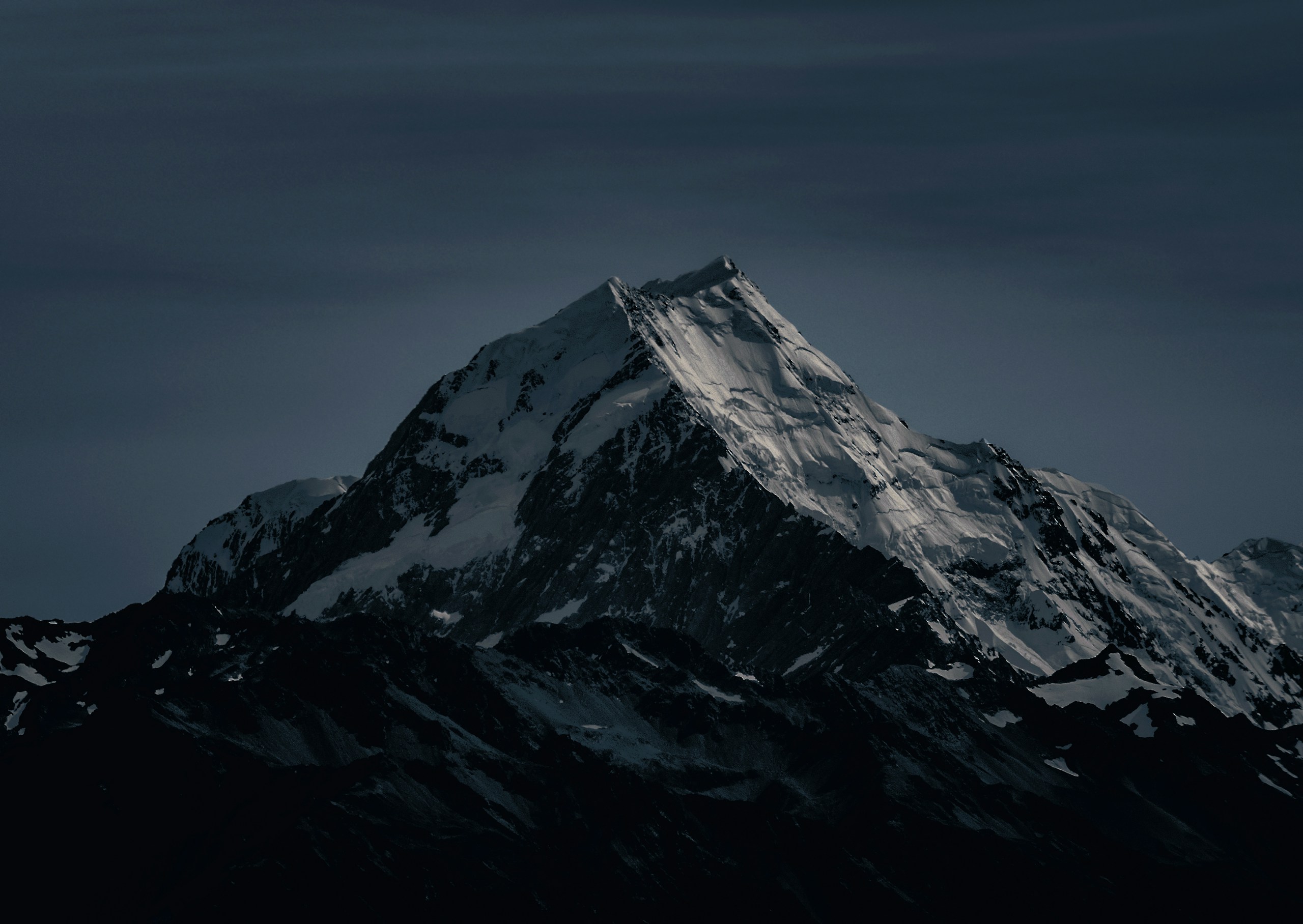 Snow-covered mountain peak under a dark sky HD Wallpaper