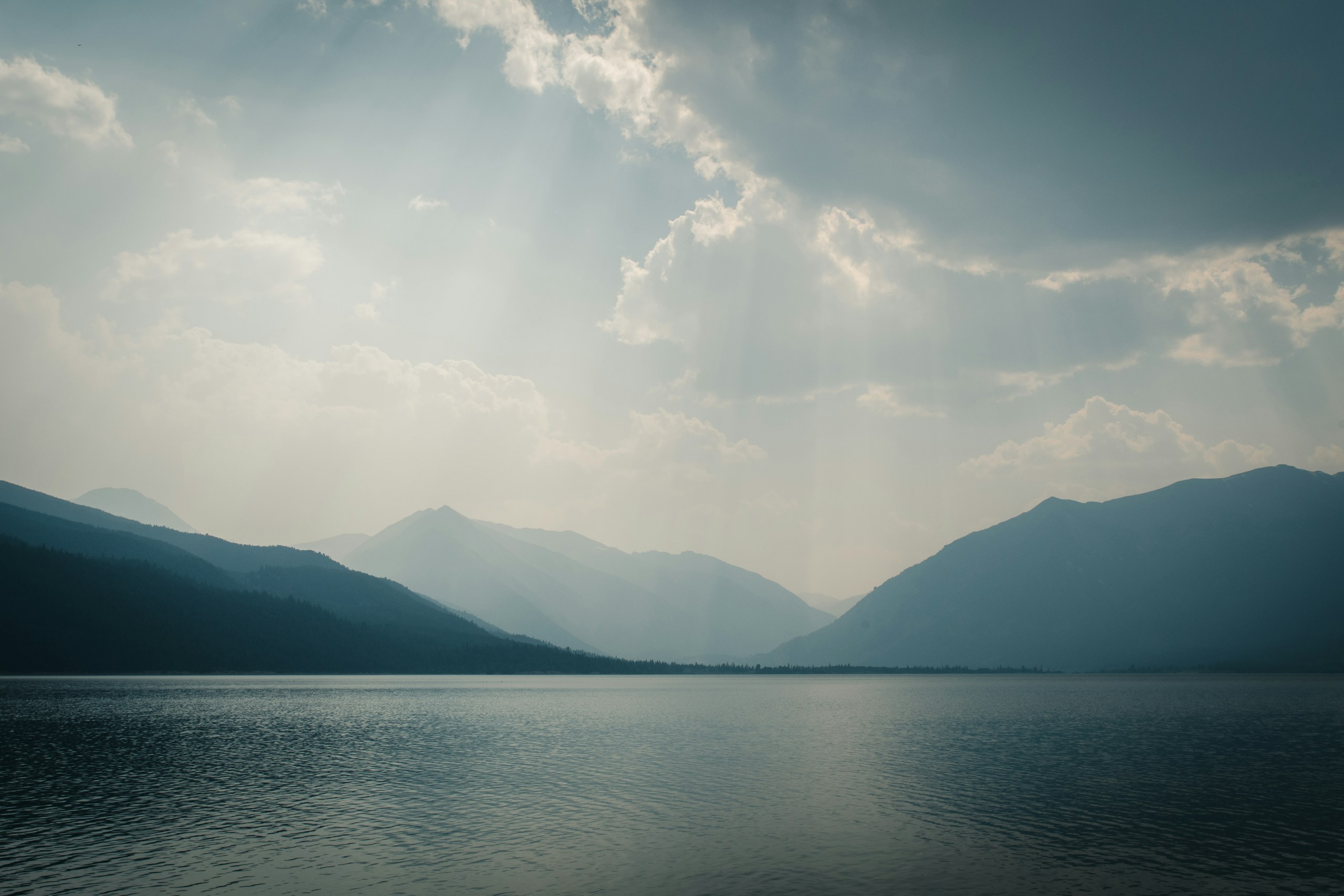 Misty mountains reflected in a calm lake under a cloudy sky HD Wallpaper