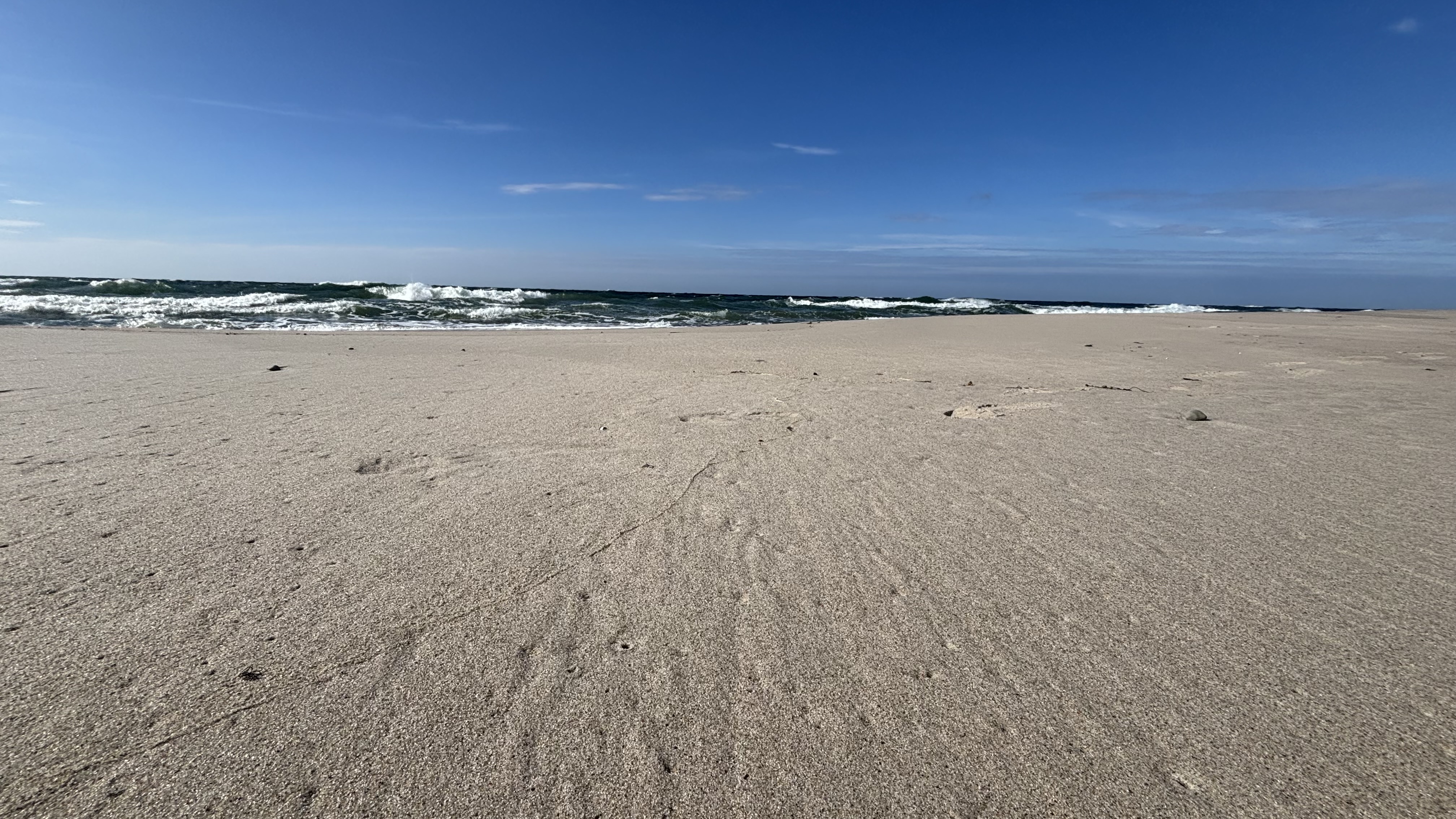Sandy beach with ocean waves under a blue sky HD Wallpaper