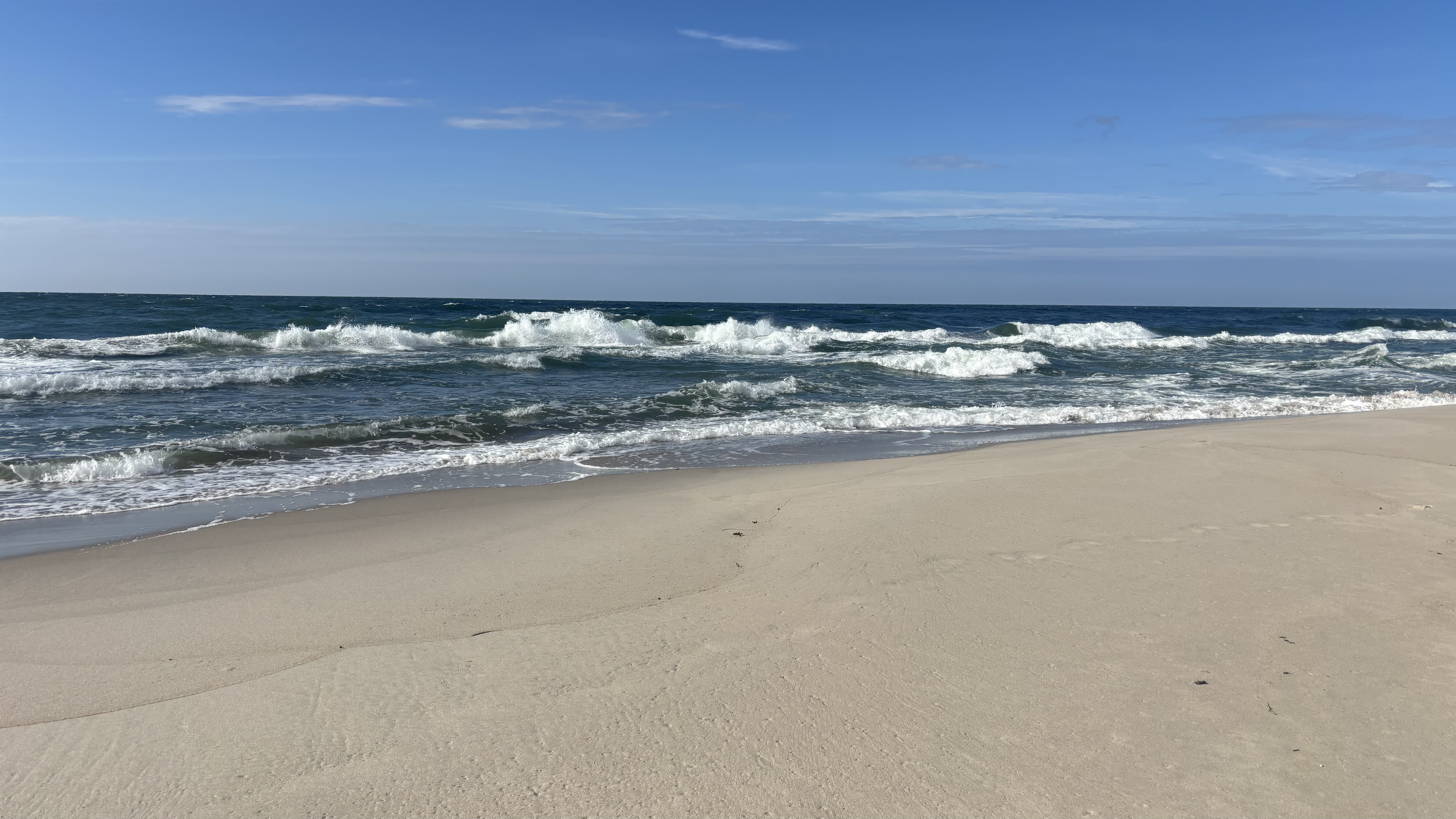 Ocean waves crashing on a sandy beach under a blue sky. HD Wallpaper