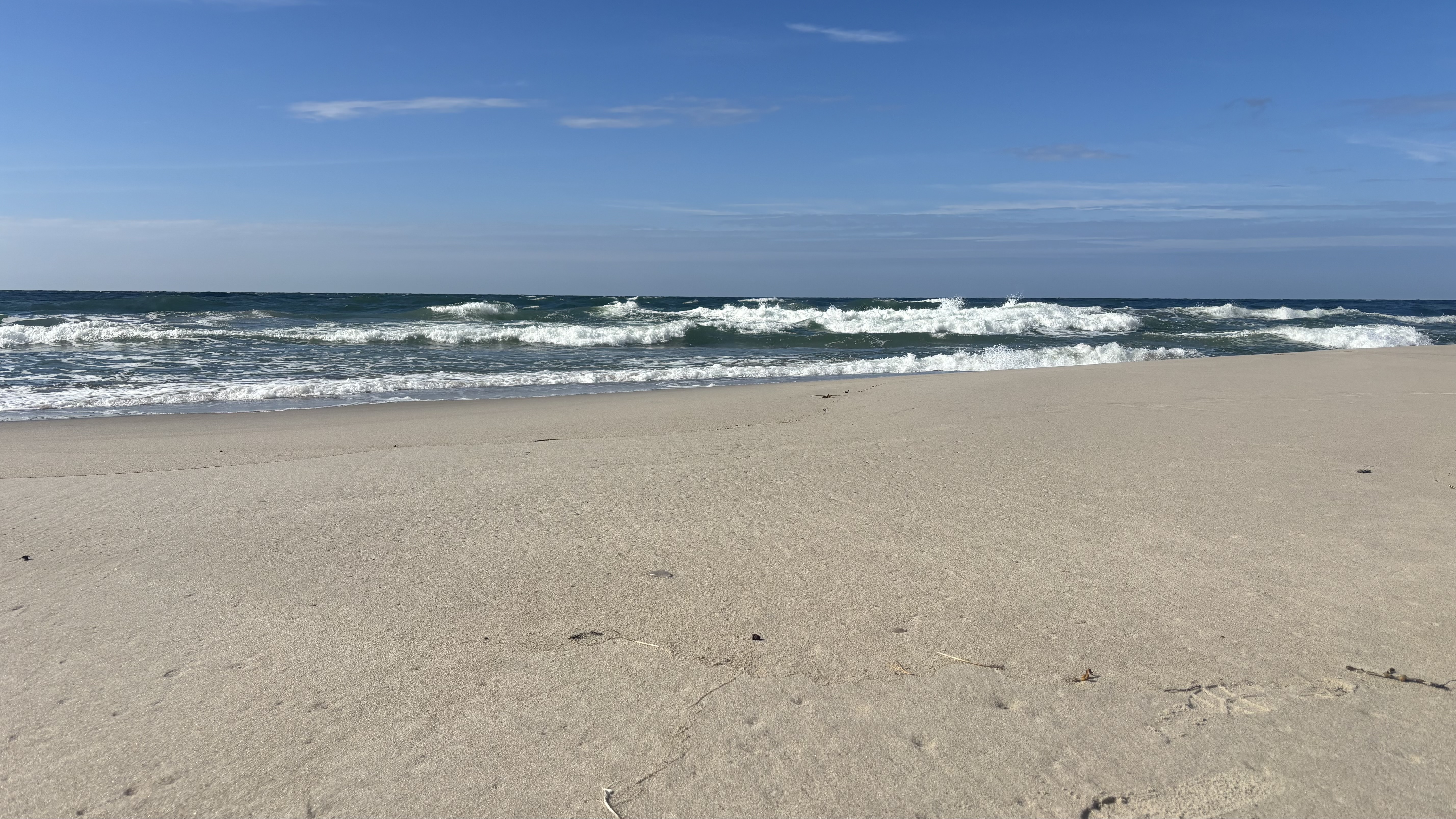 Sandy beach with waves under a blue sky HD Wallpaper
