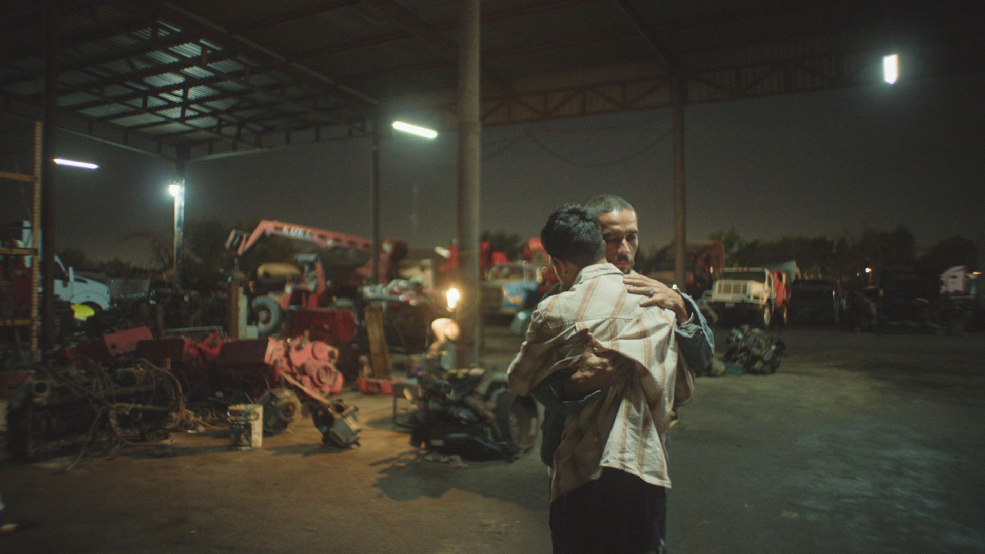Two men embrace in a junkyard at night HD Wallpaper