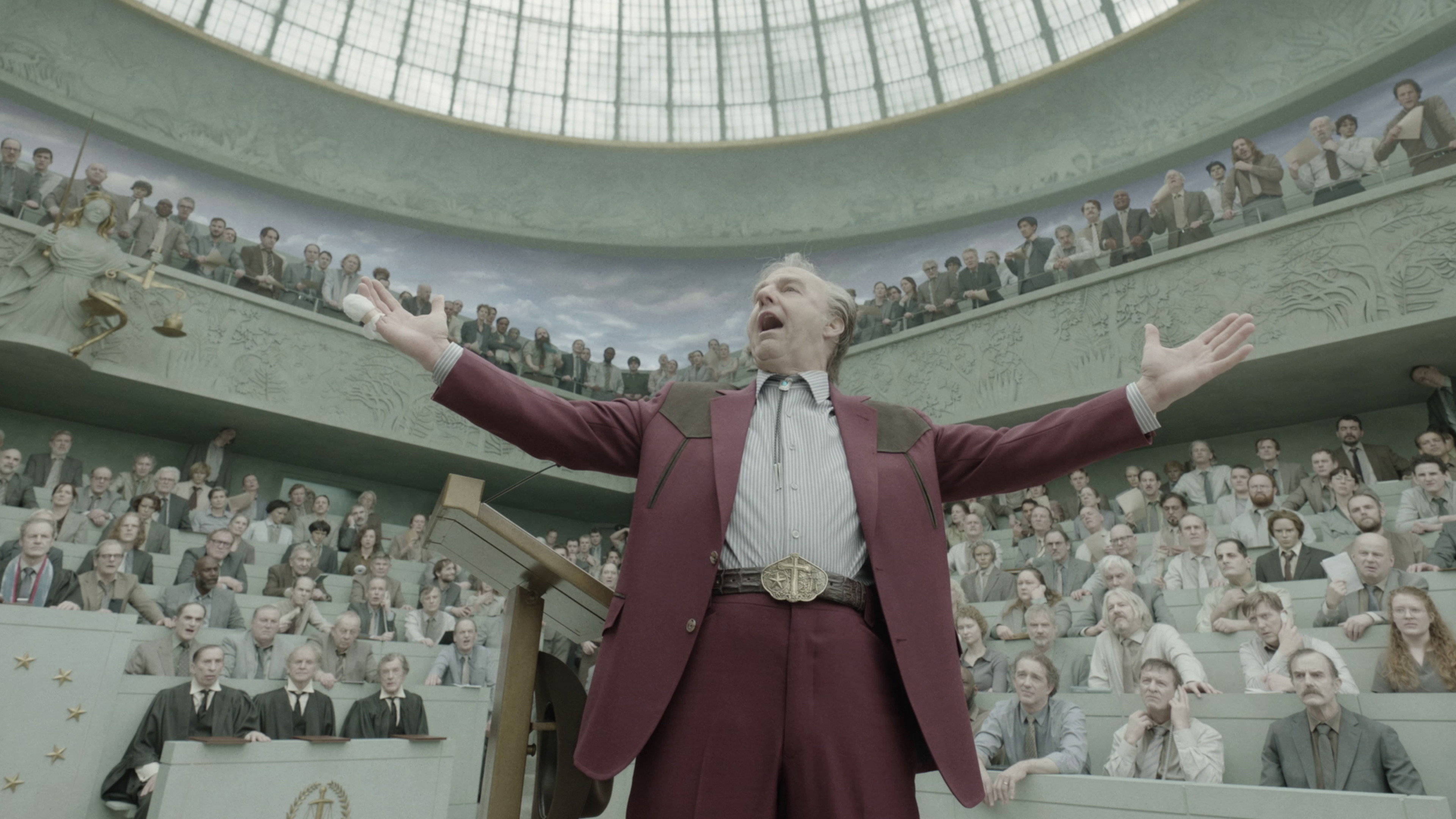 Man speaking to an audience in a grand hall HD Wallpaper