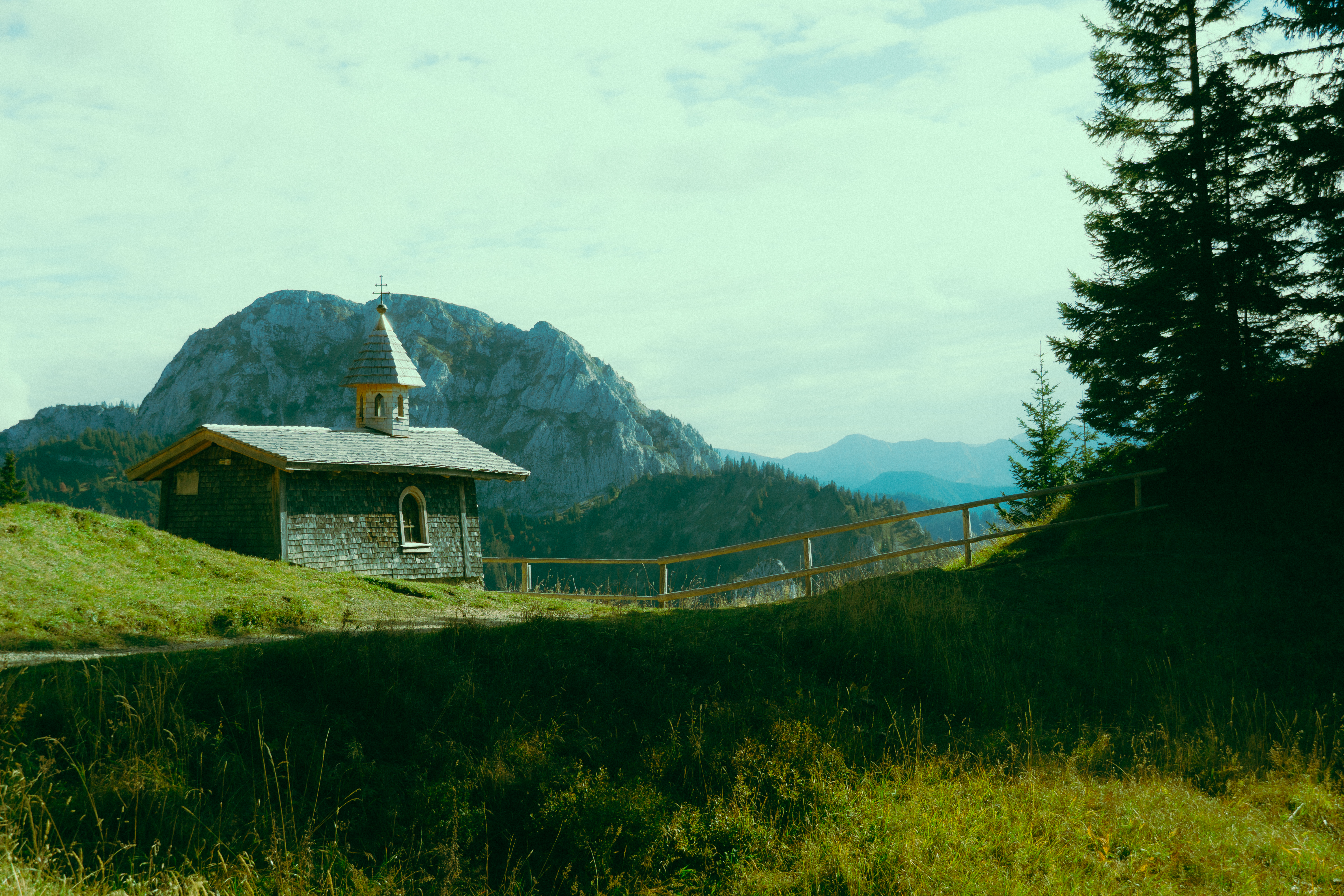 Small chapel on a grassy hill with mountains HD Wallpaper