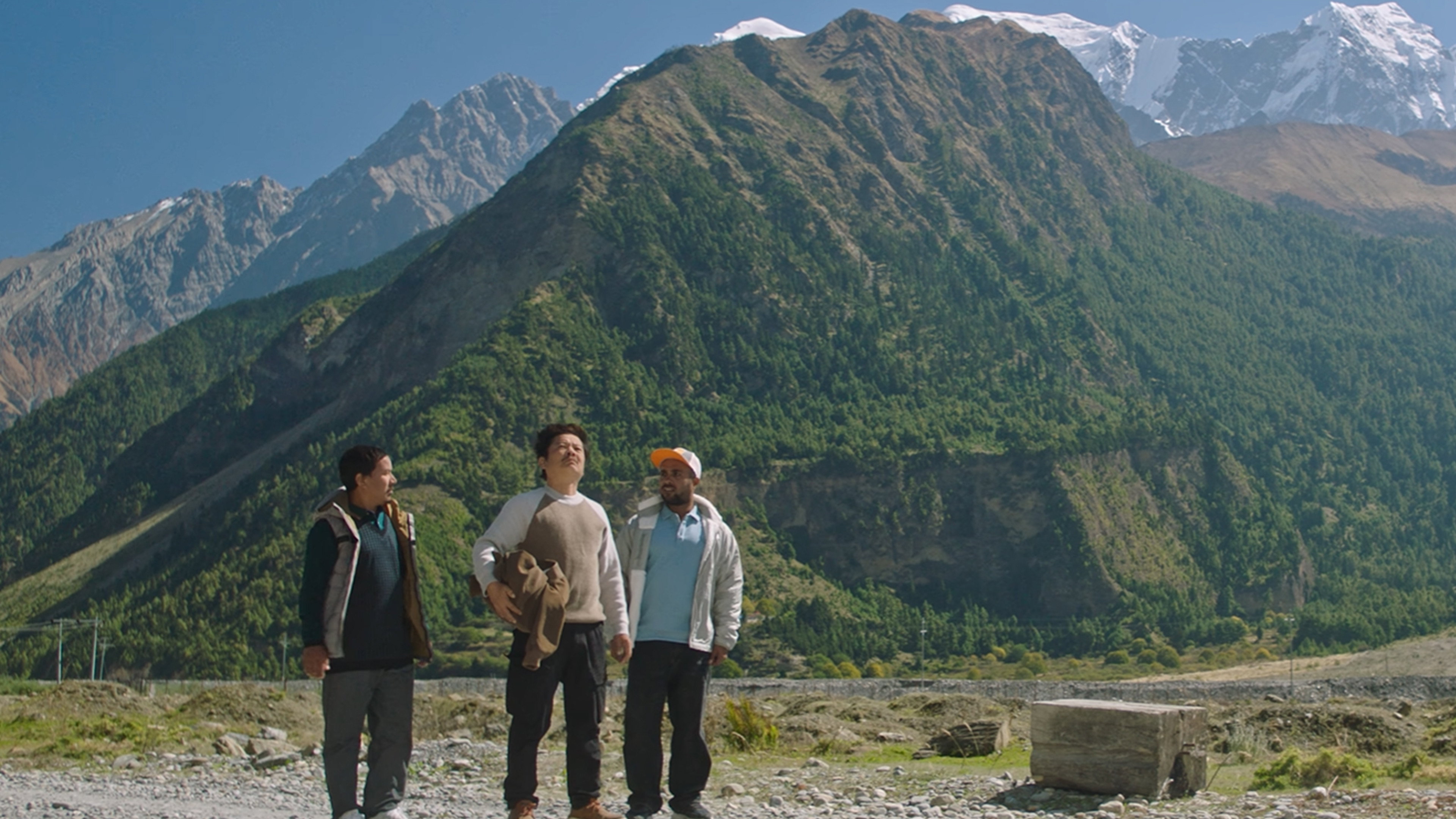 Three men stand before a majestic mountain range HD Wallpaper