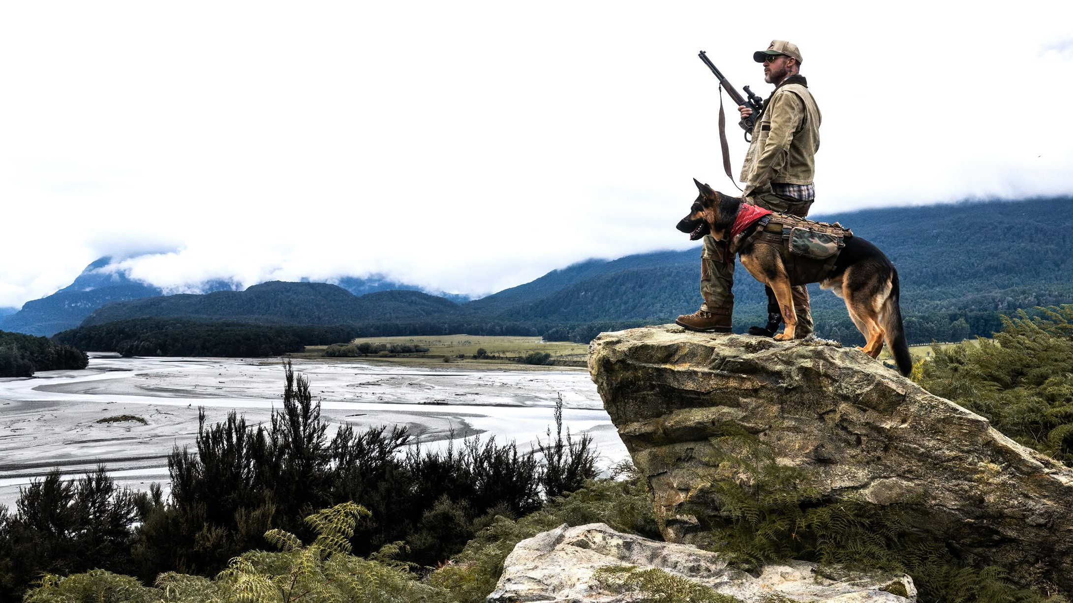 Man with dog on cliff overlooking river valley HD Wallpaper