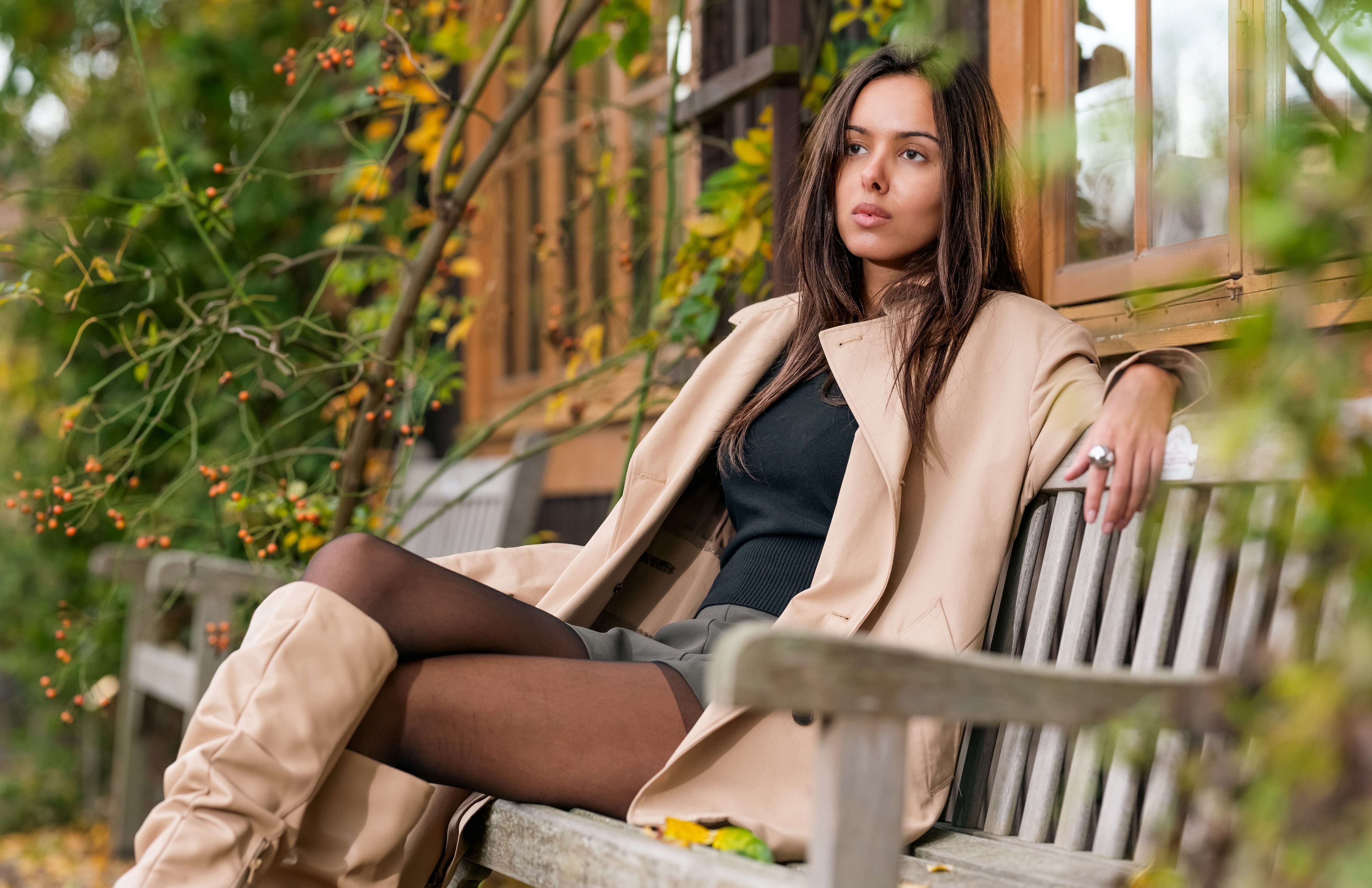 Woman in trench coat sitting on a bench outdoors HD Wallpaper