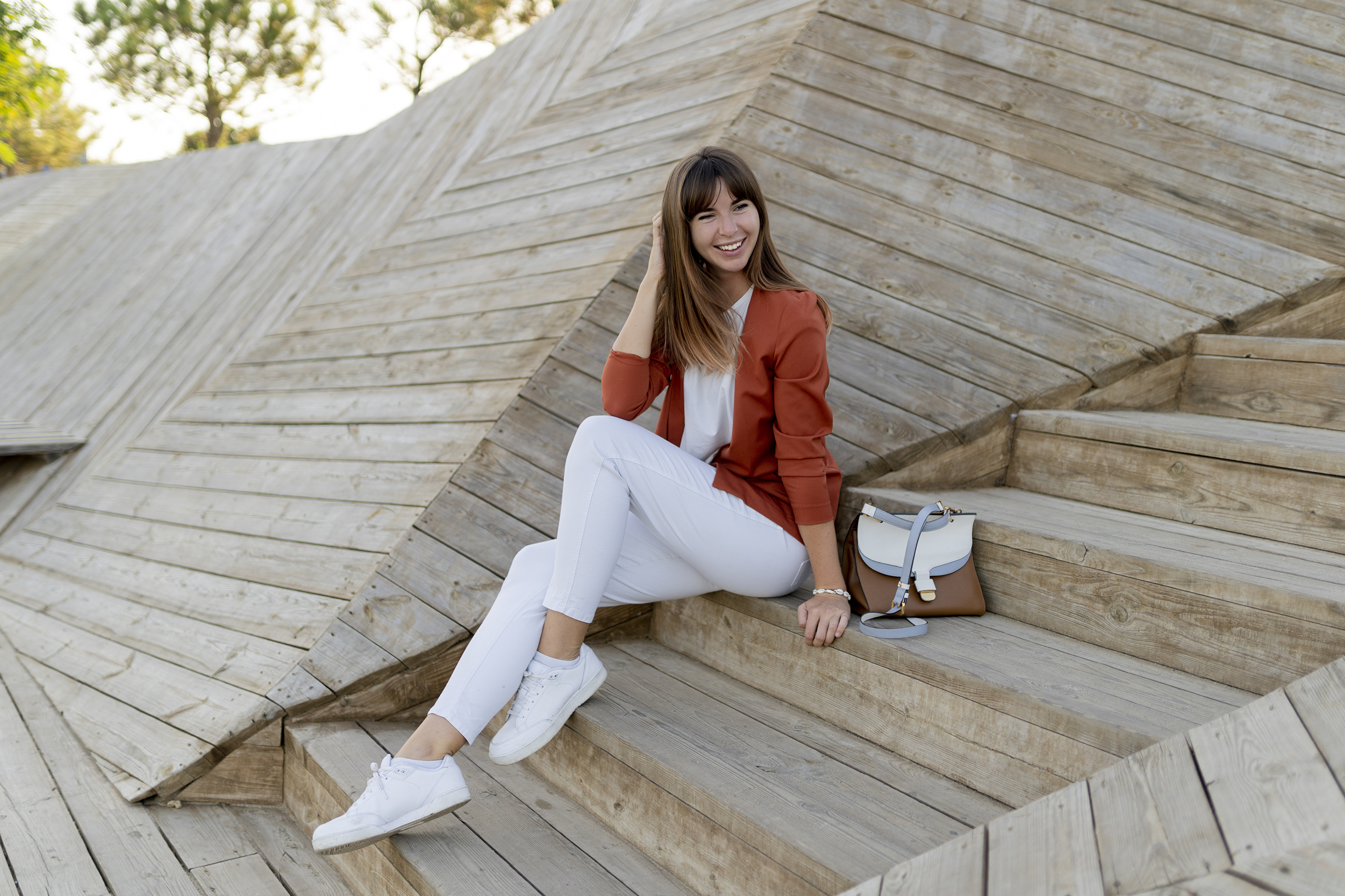 Woman in orange blazer and white pants sitting on wooden stairs HD Wallpaper
