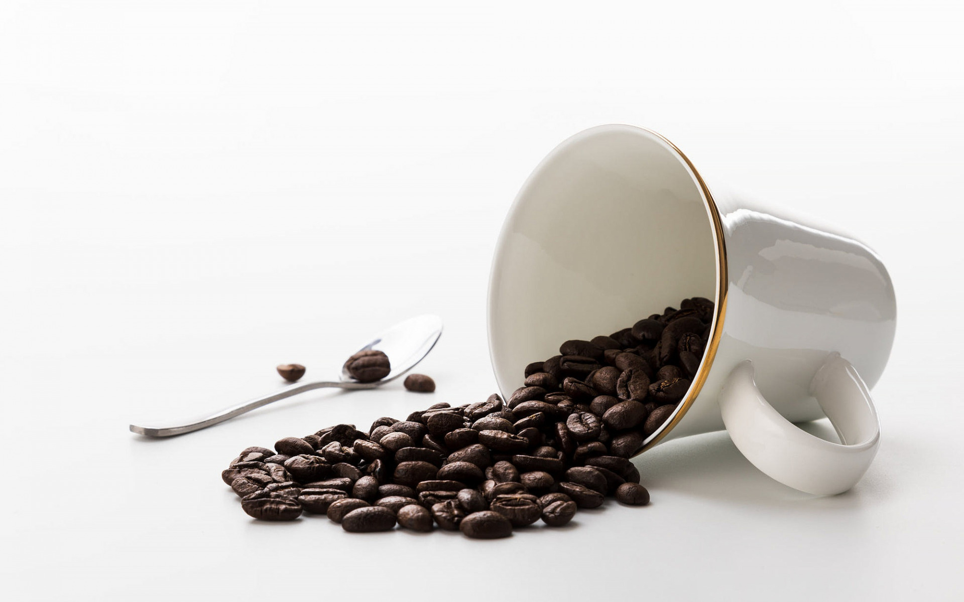 Coffee beans spilling from a mug onto a spoon and surface HD Wallpaper