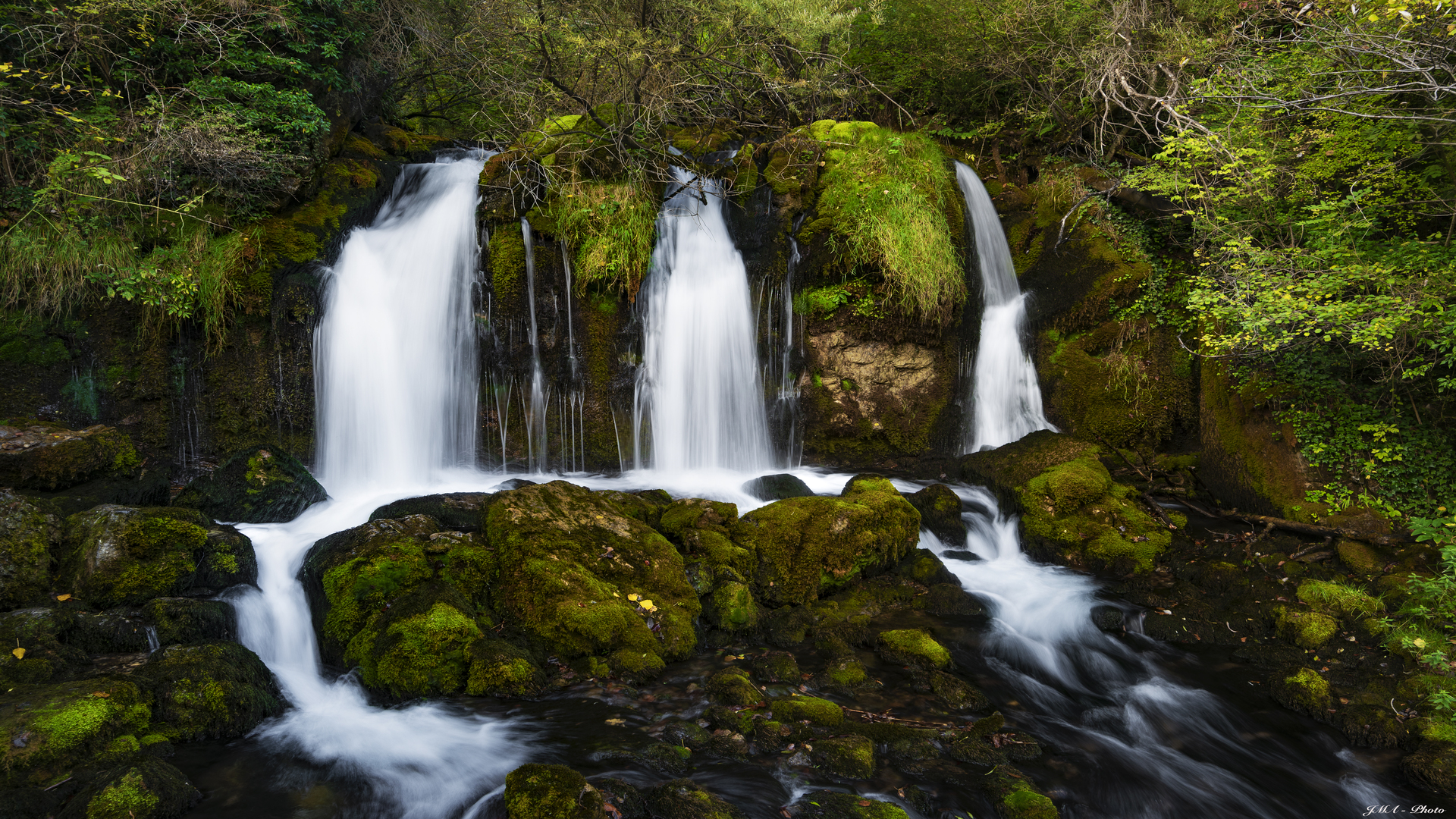 Waterfall cascading over moss-covered rocks in a forest HD Wallpaper