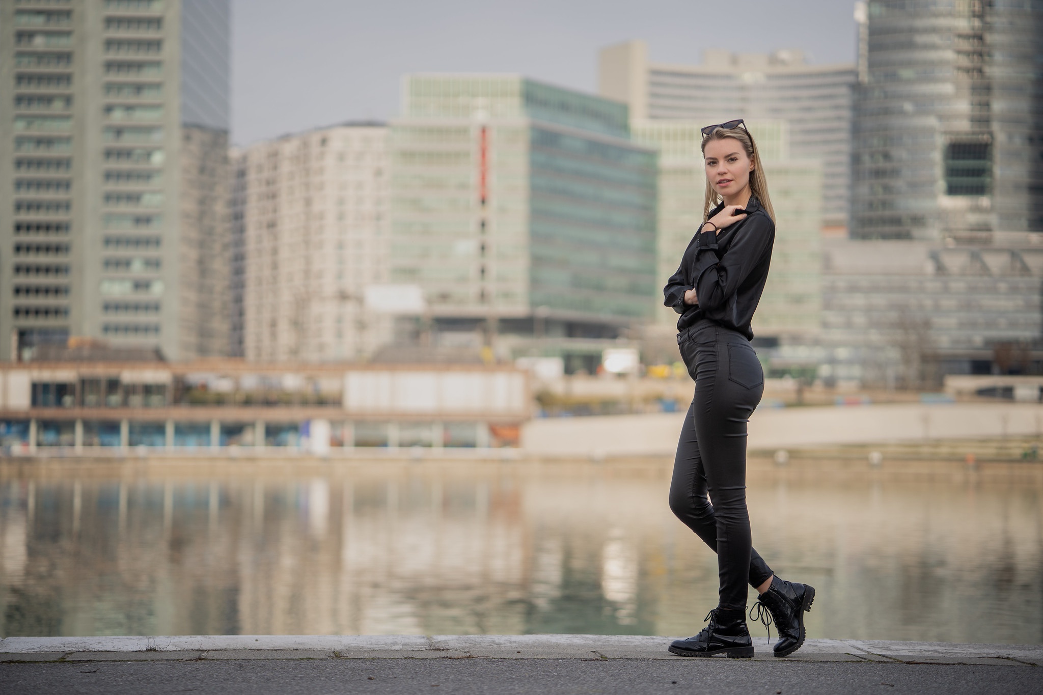 Woman in black standing by a river with city buildings HD Wallpaper
