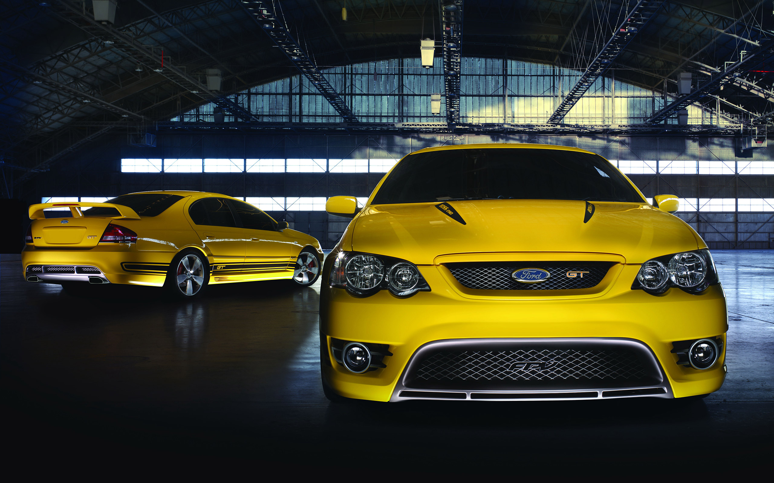 Two yellow Ford FPV BFII GT sedans in a hangar HD Wallpaper
