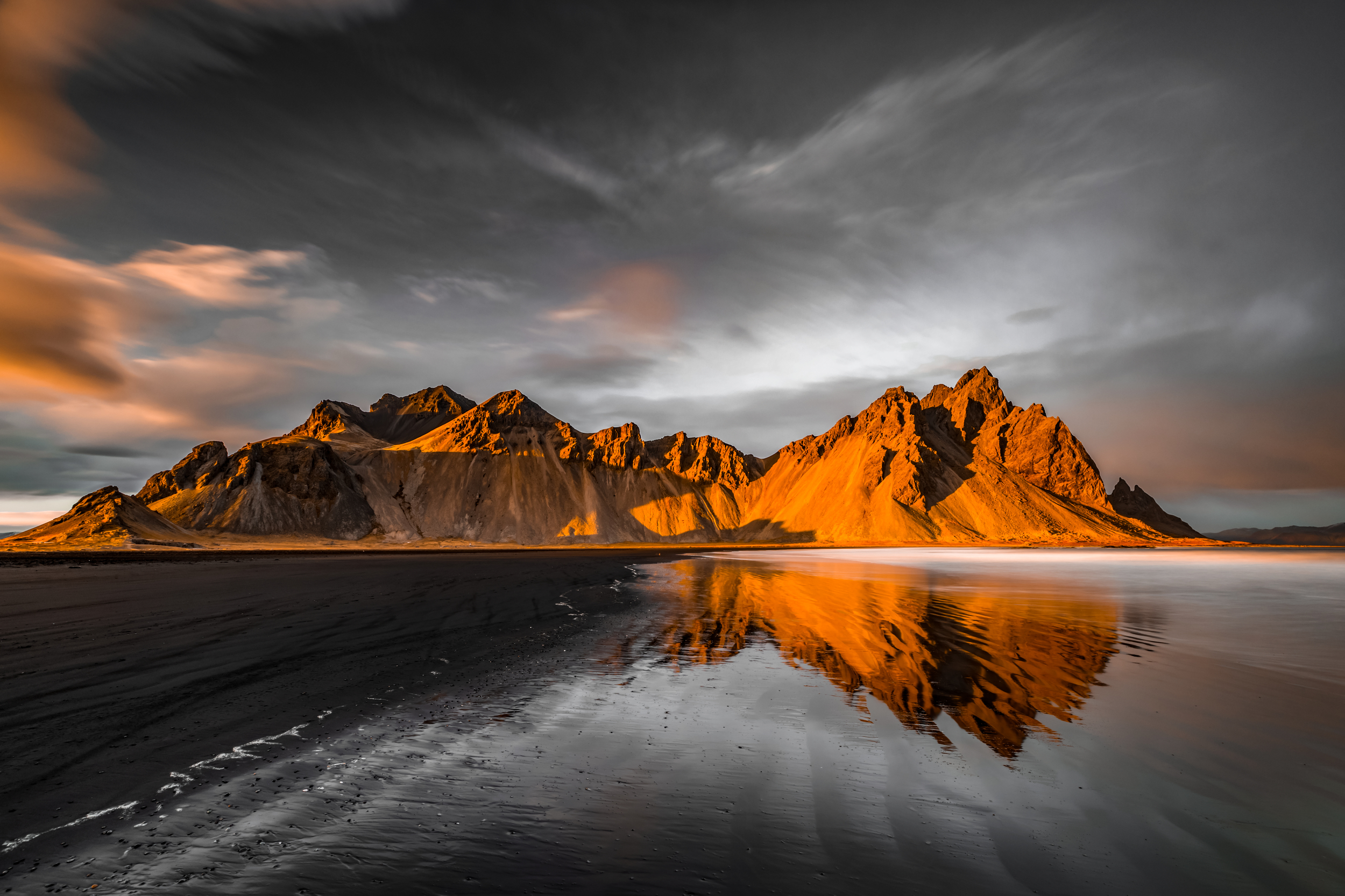 Mountain range reflecting on wet black sand beach at sunset HD Wallpaper