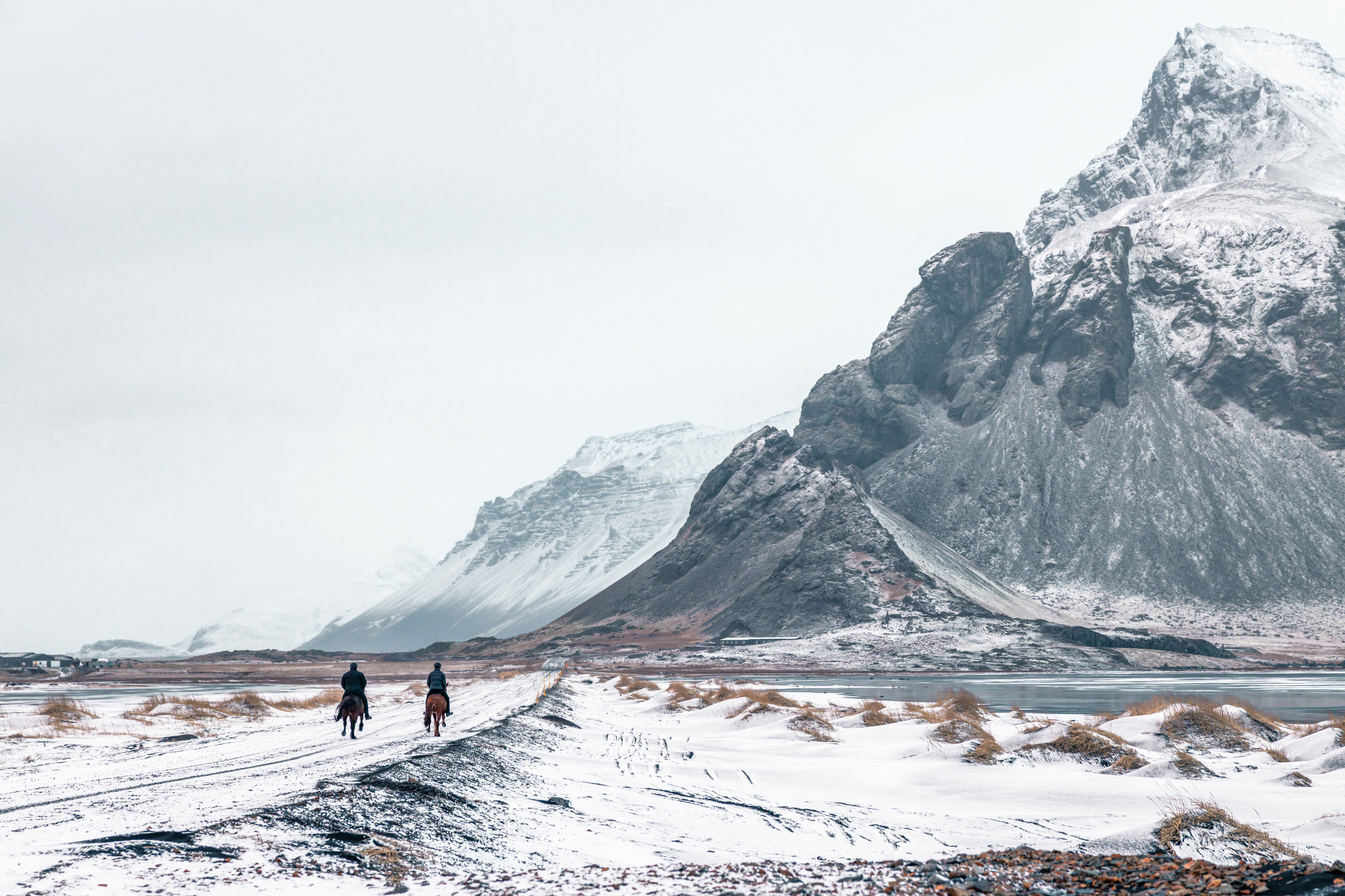 Two people on horseback on a snowy path with mountains HD Wallpaper