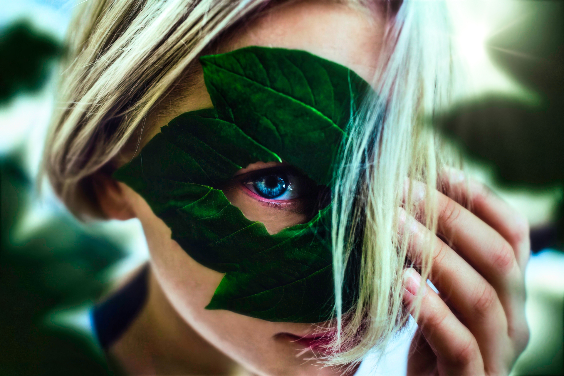 Woman with blue eyes and blonde hair covered by green leaves HD Wallpaper