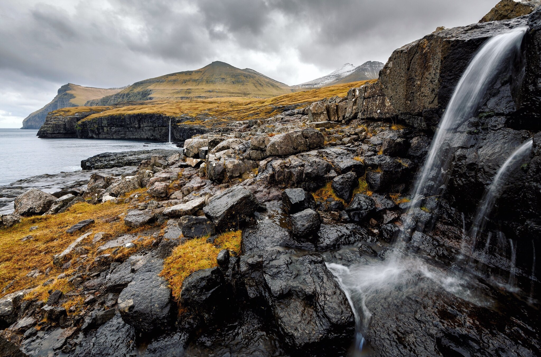 Waterfall cascading over rocks on the Faroe Islands coastline HD Wallpaper