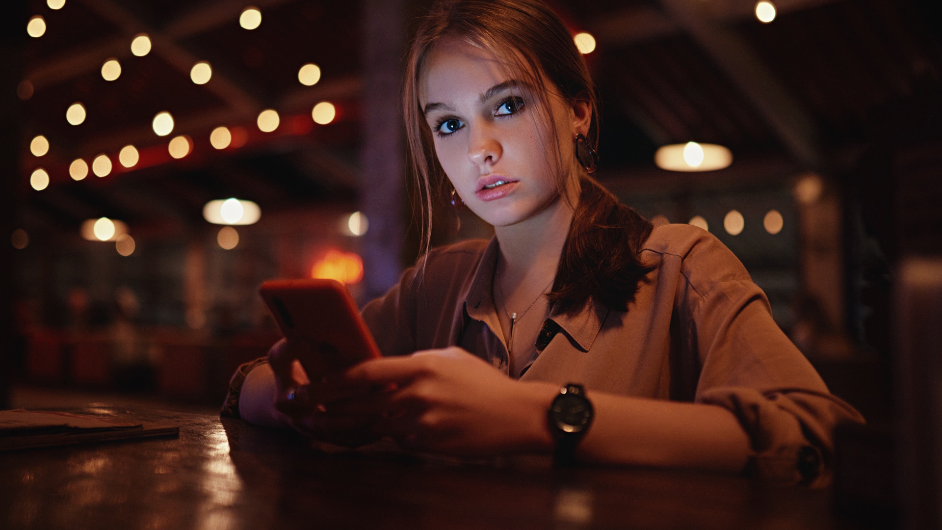 Woman holding a smartphone in a dimly lit room HD Wallpaper
