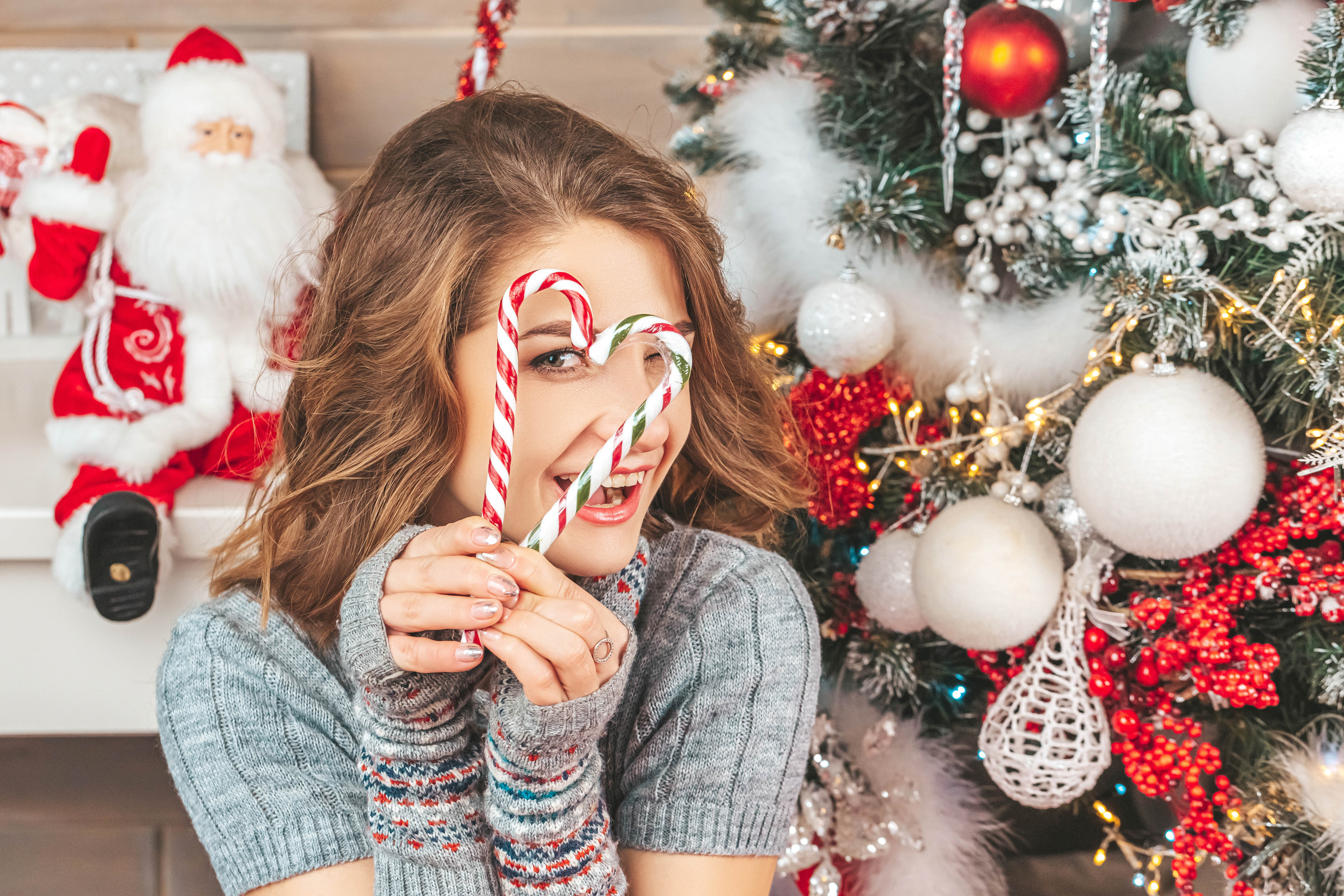 Woman holding candy canes in front of Christmas tree HD Wallpaper
