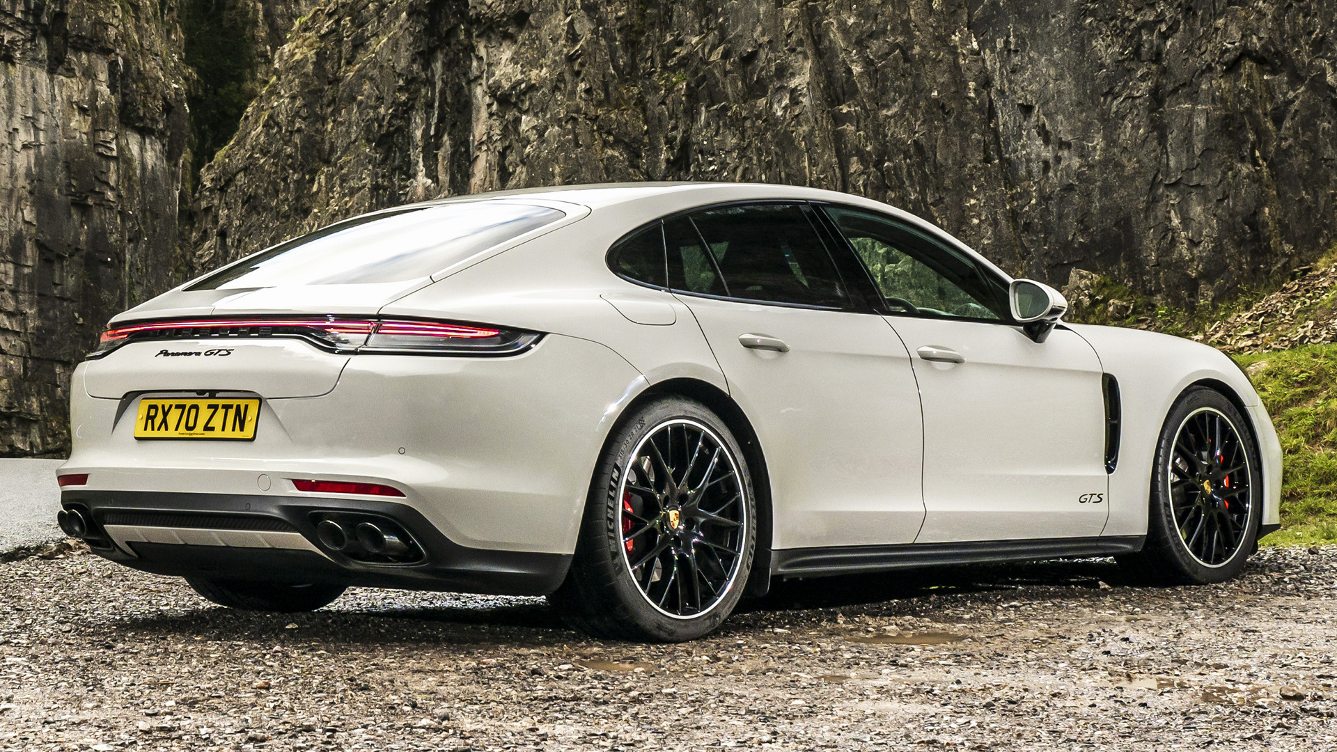 White Porsche Panamera GTS parked on gravel near rocks HD Wallpaper