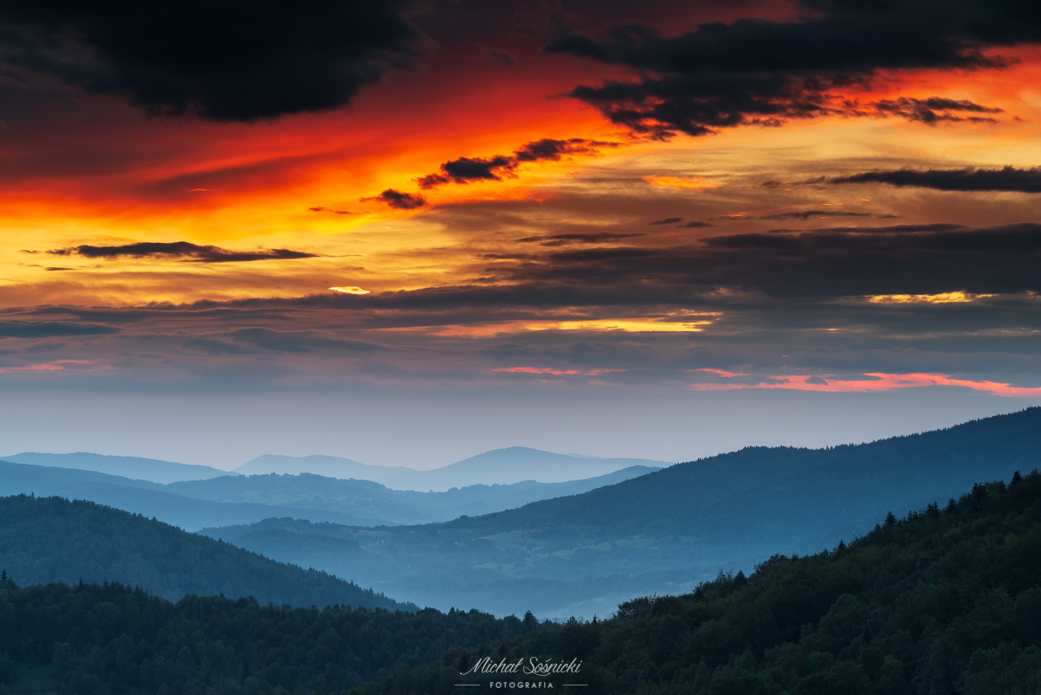 Dramatic sunset over layered mountains and forests HD Wallpaper
