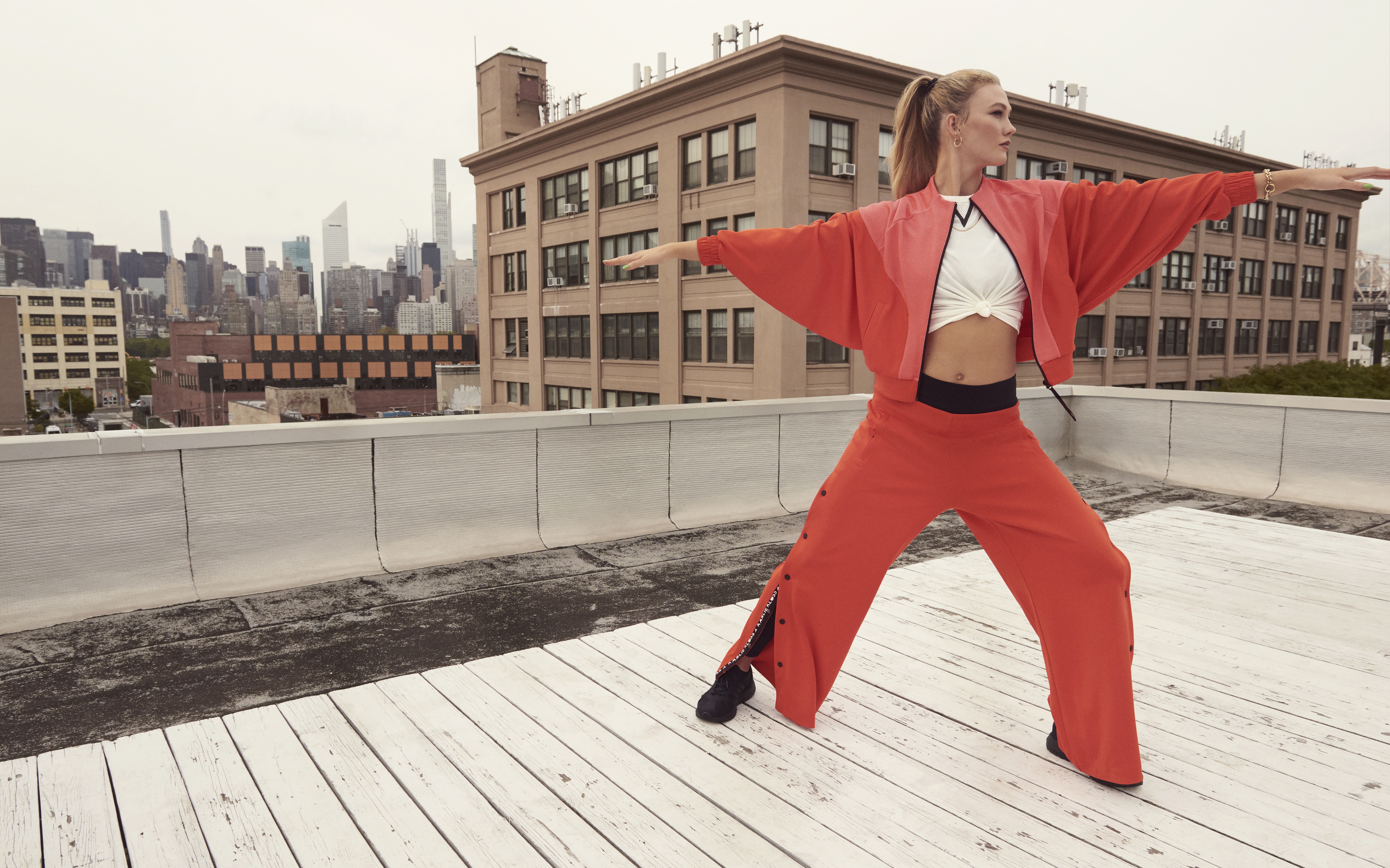 Karlie Kloss in orange athletic wear on a rooftop HD Wallpaper
