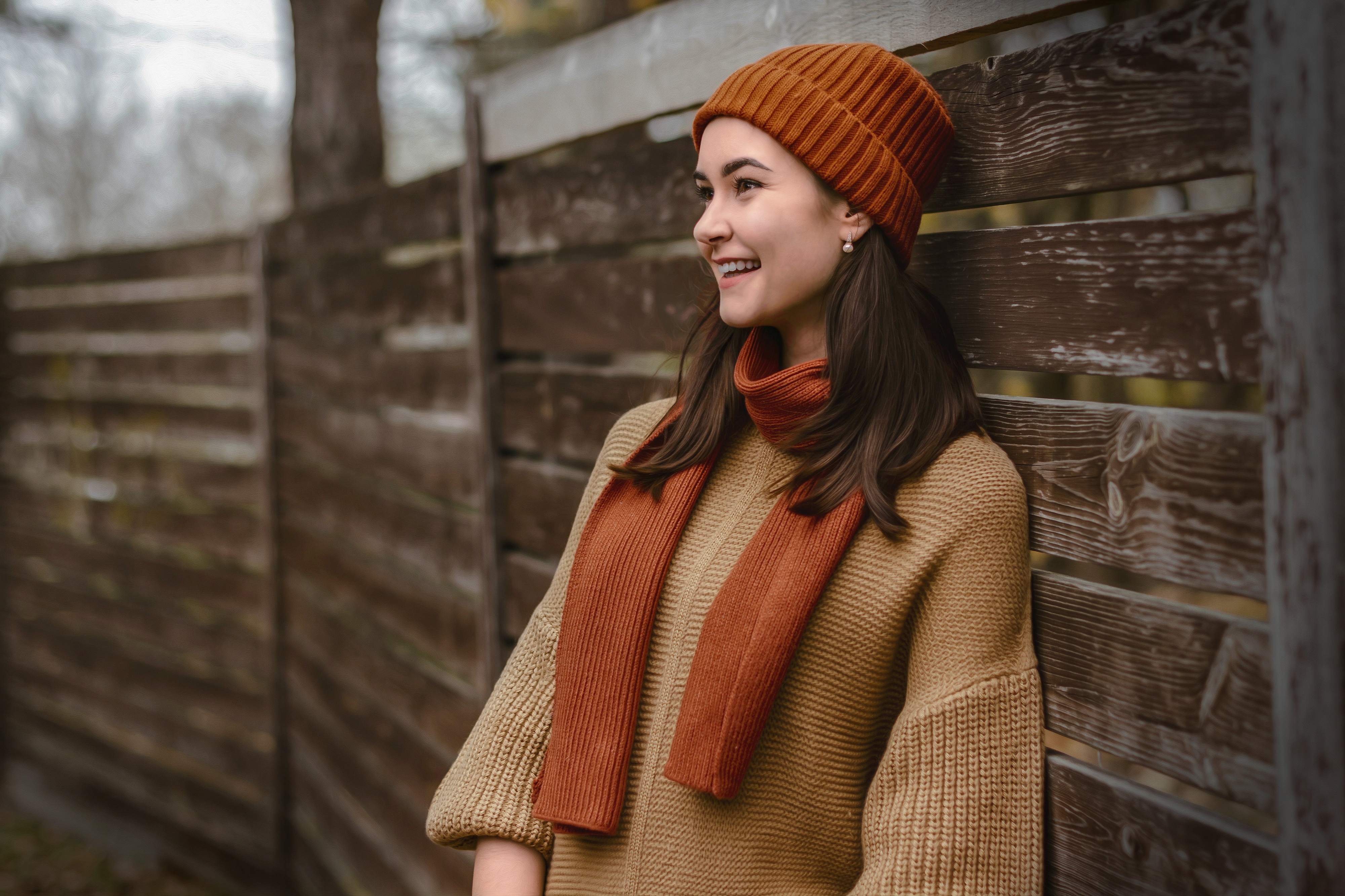 Woman in orange beanie and scarf leaning on fence HD Wallpaper