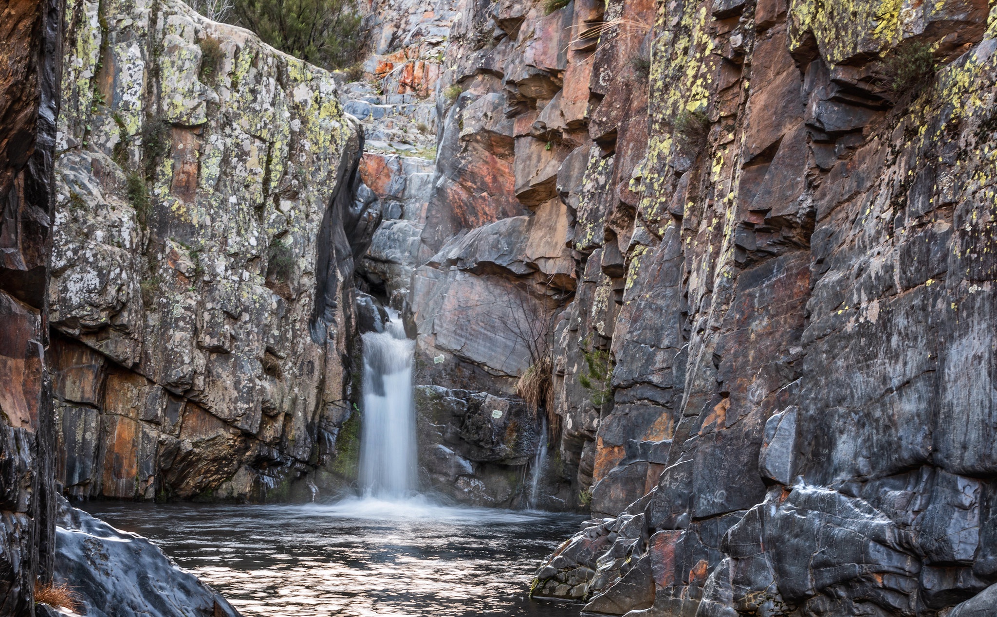 Waterfall cascading into a pool surrounded by rocky cliffs HD Wallpaper