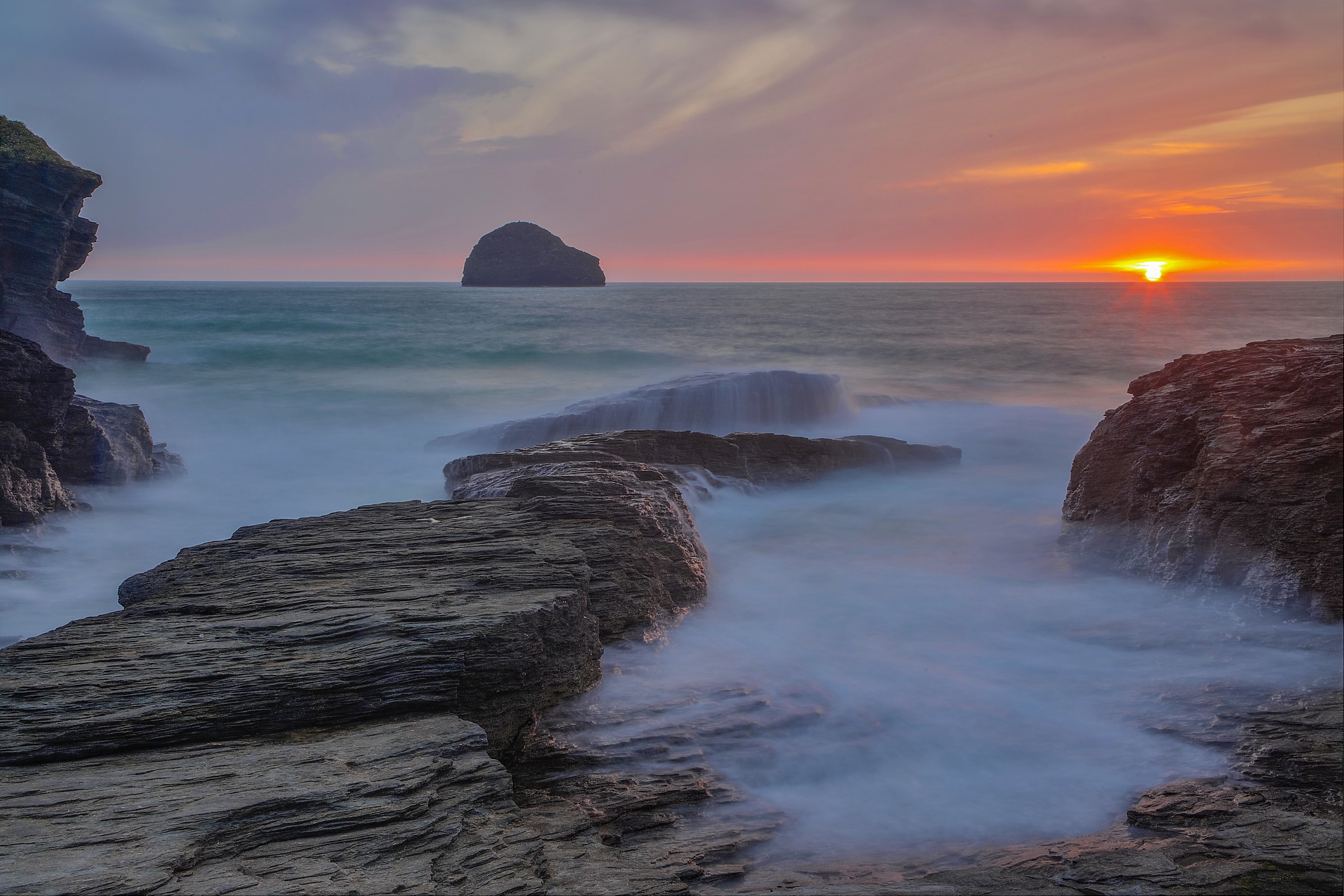 Sunset over the ocean with rocks and a small island HD Wallpaper