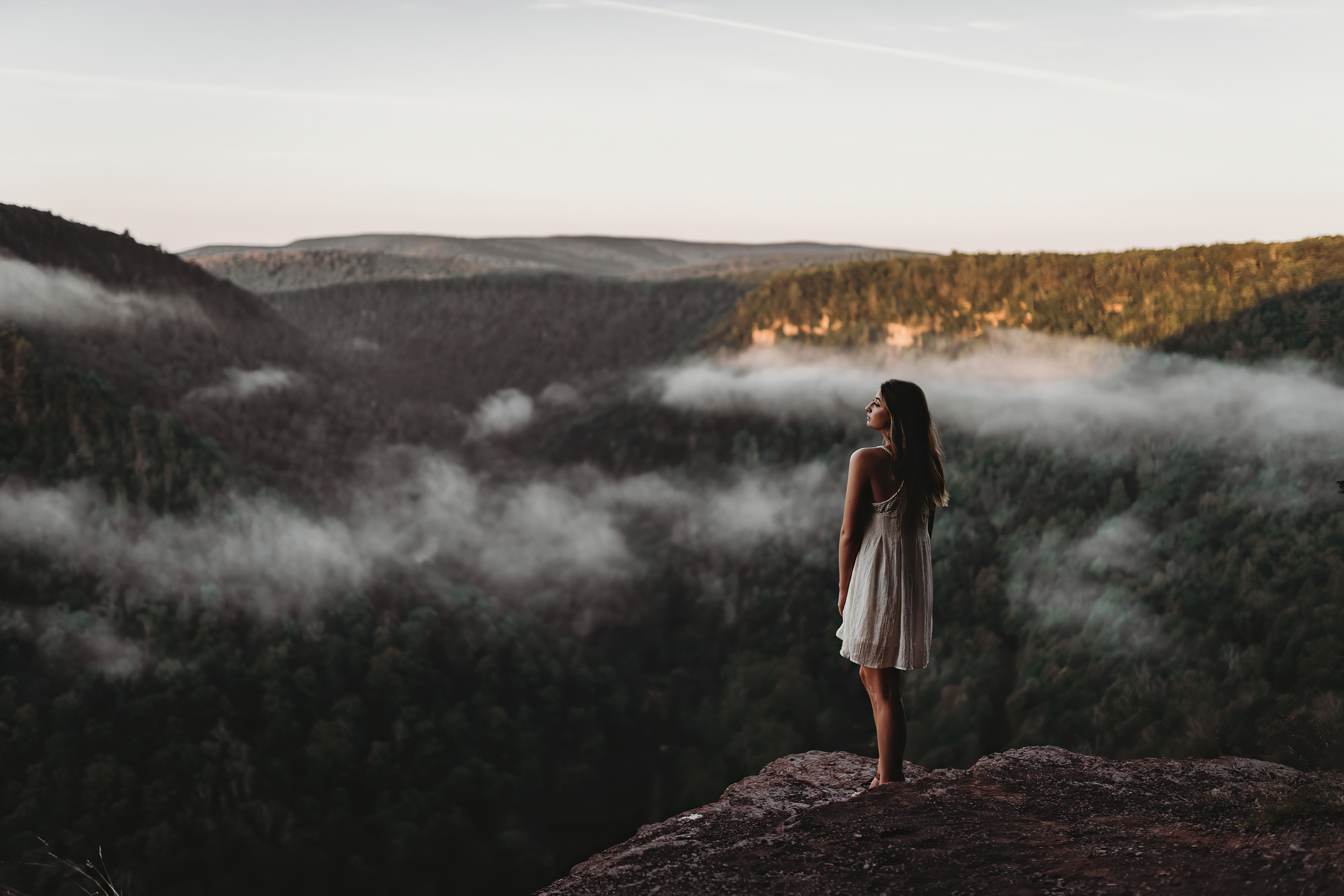 Girl in white dress on cliff overlooking foggy mountains HD Wallpaper