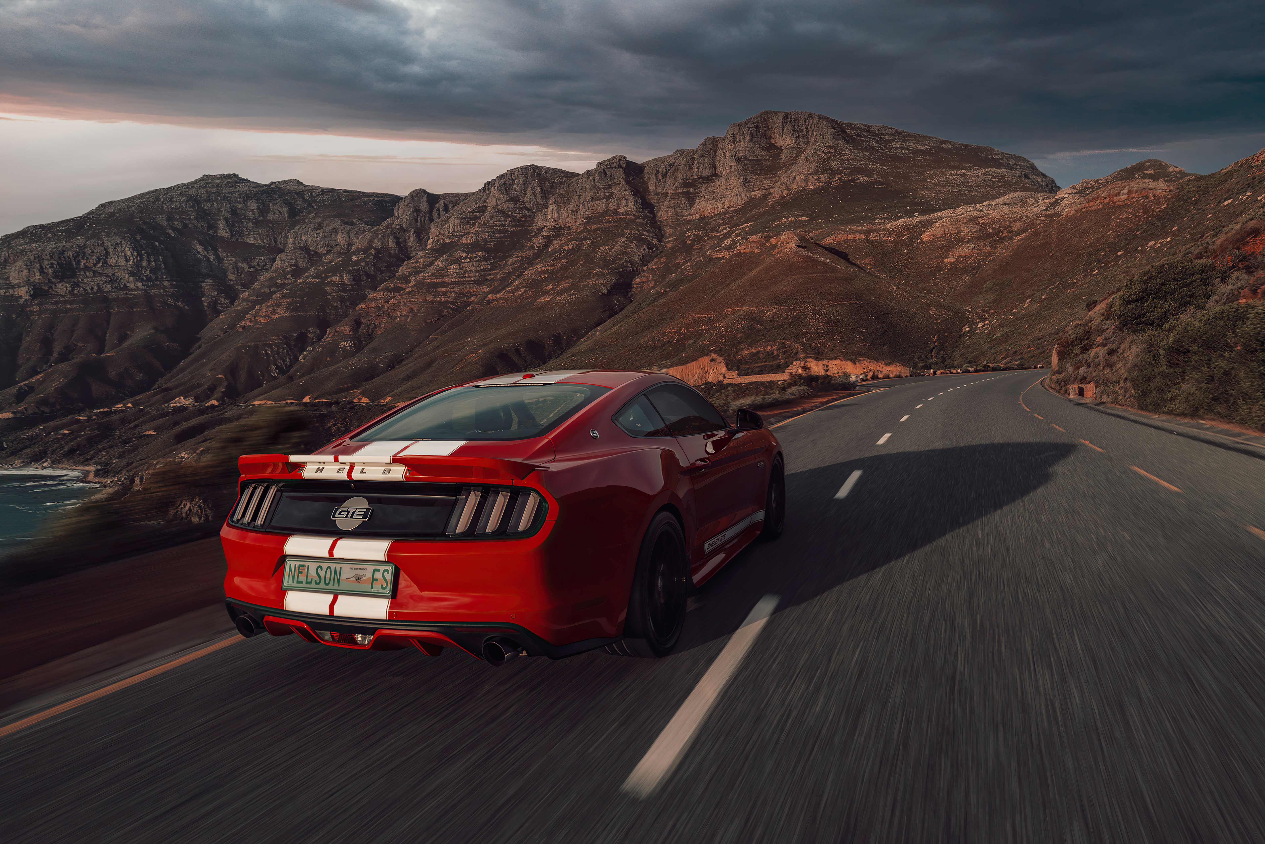 Red Ford Mustang GT driving on a scenic mountain road HD Wallpaper