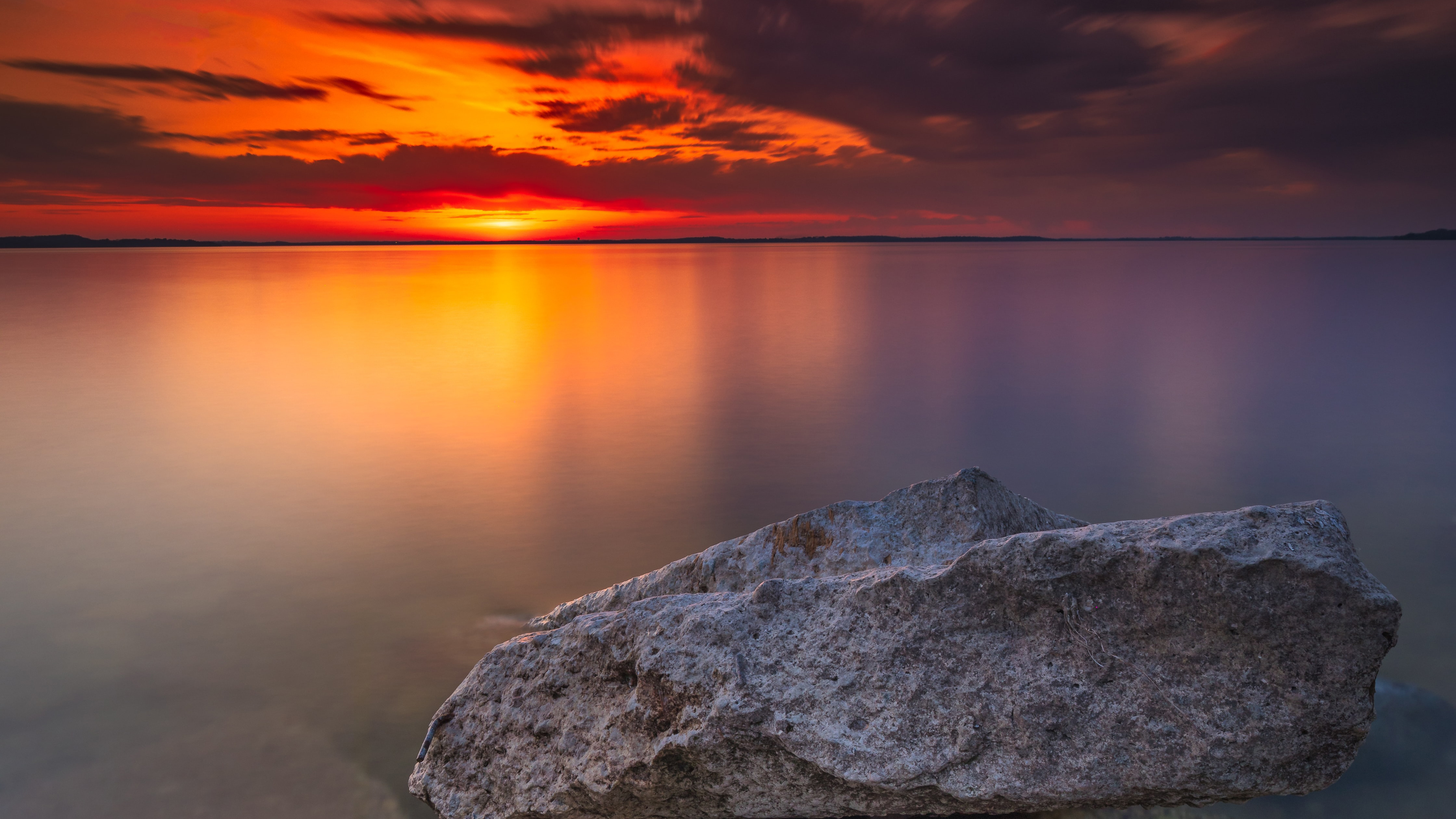 Sunset over a calm lake with rocks in the foreground HD Wallpaper