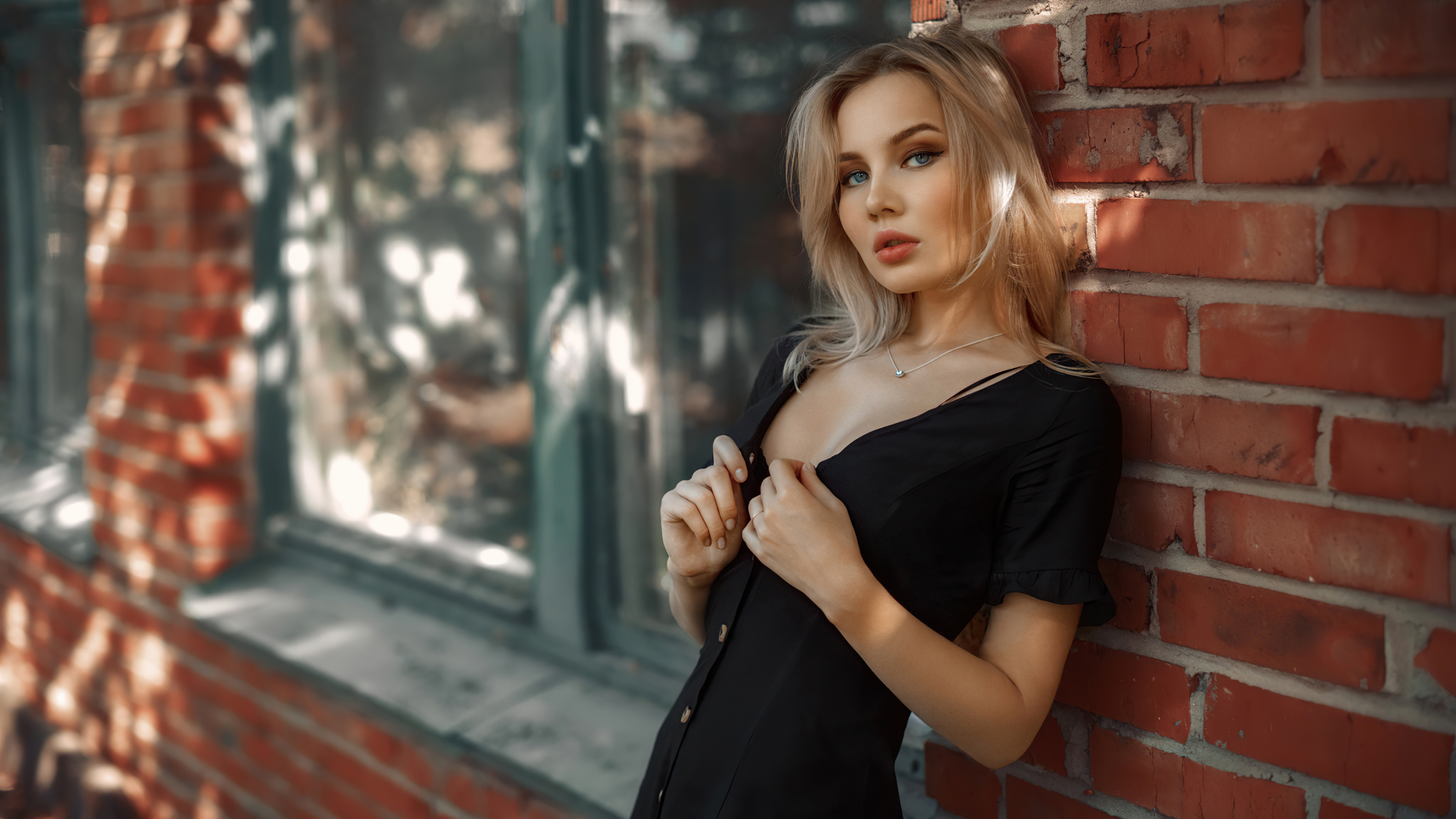 Blonde woman in black dress leaning against brick wall HD Wallpaper