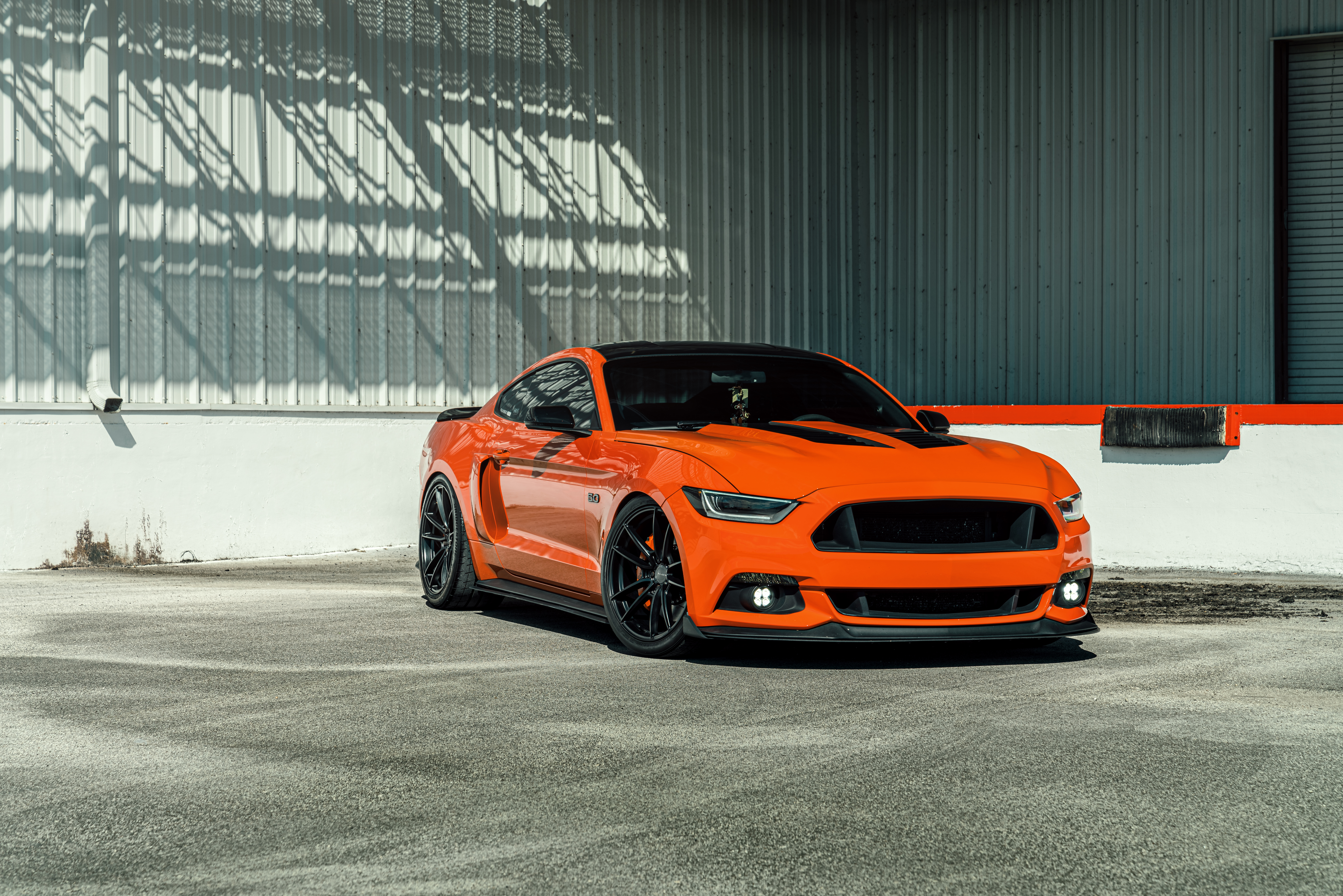 Orange Ford Mustang parked in front of a building HD Wallpaper