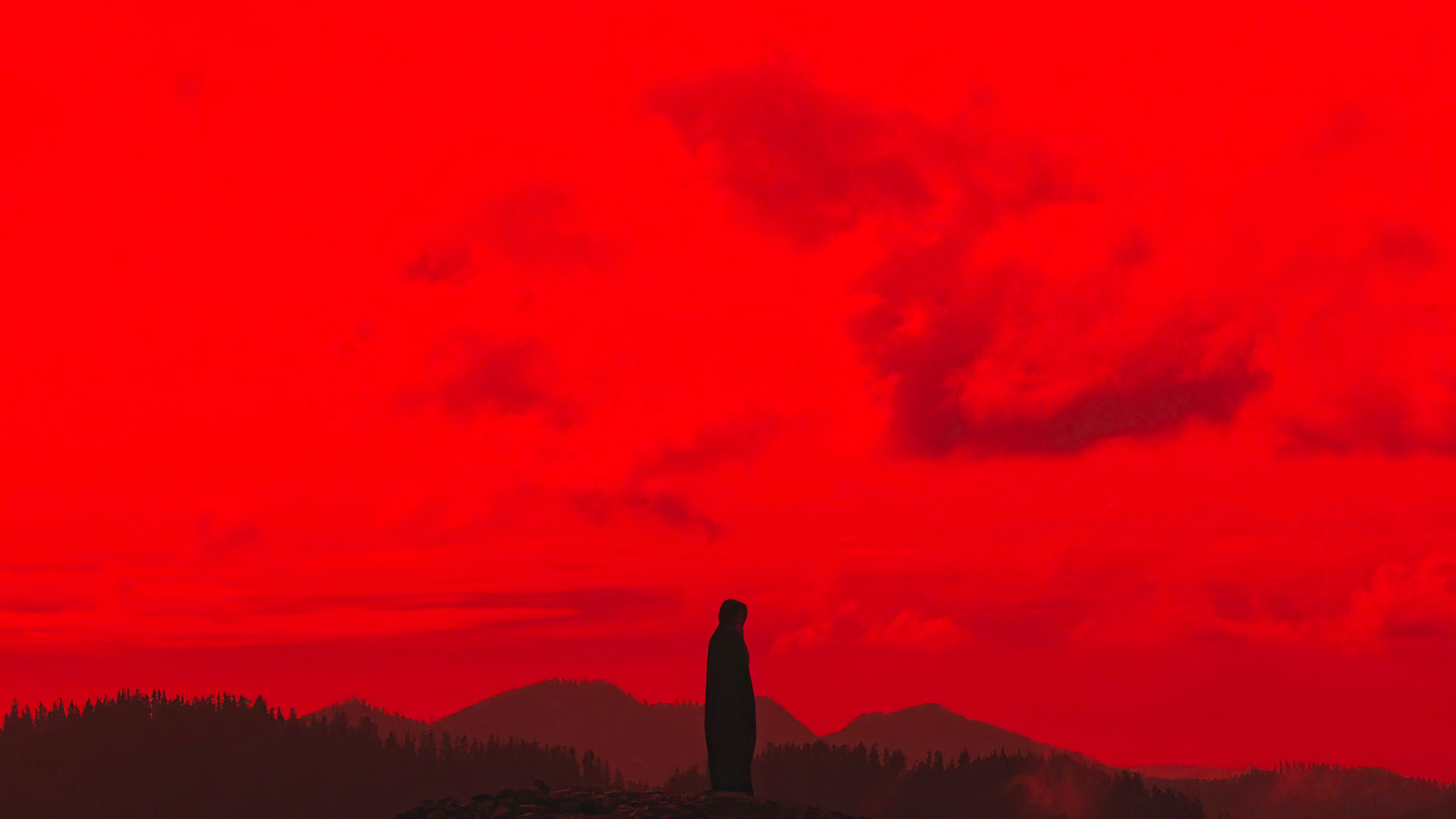 Silhouette of a person standing on a mountain peak against a red sky HD Wallpaper