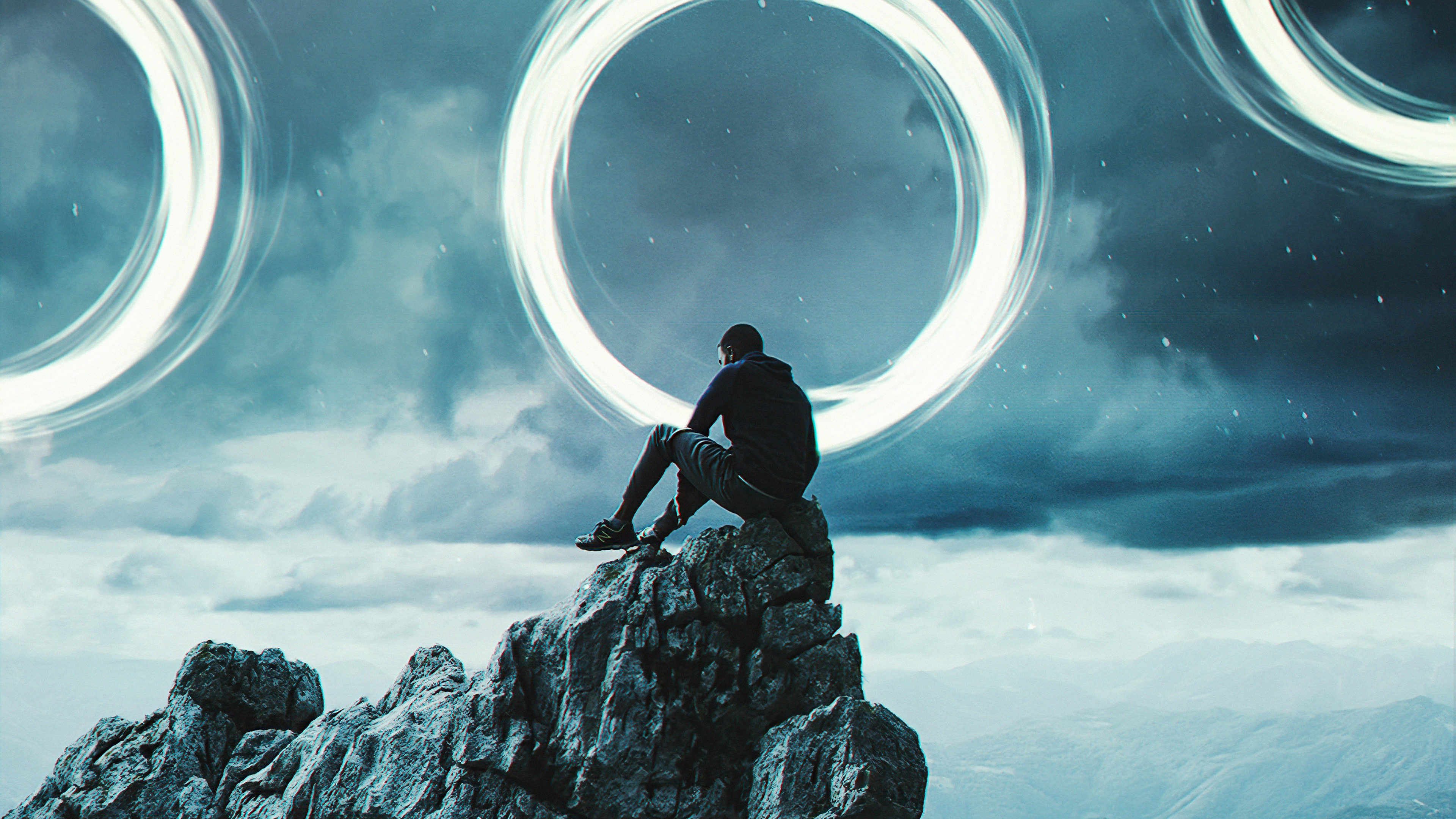 Man sitting on a rock with glowing rings in the sky HD Wallpaper