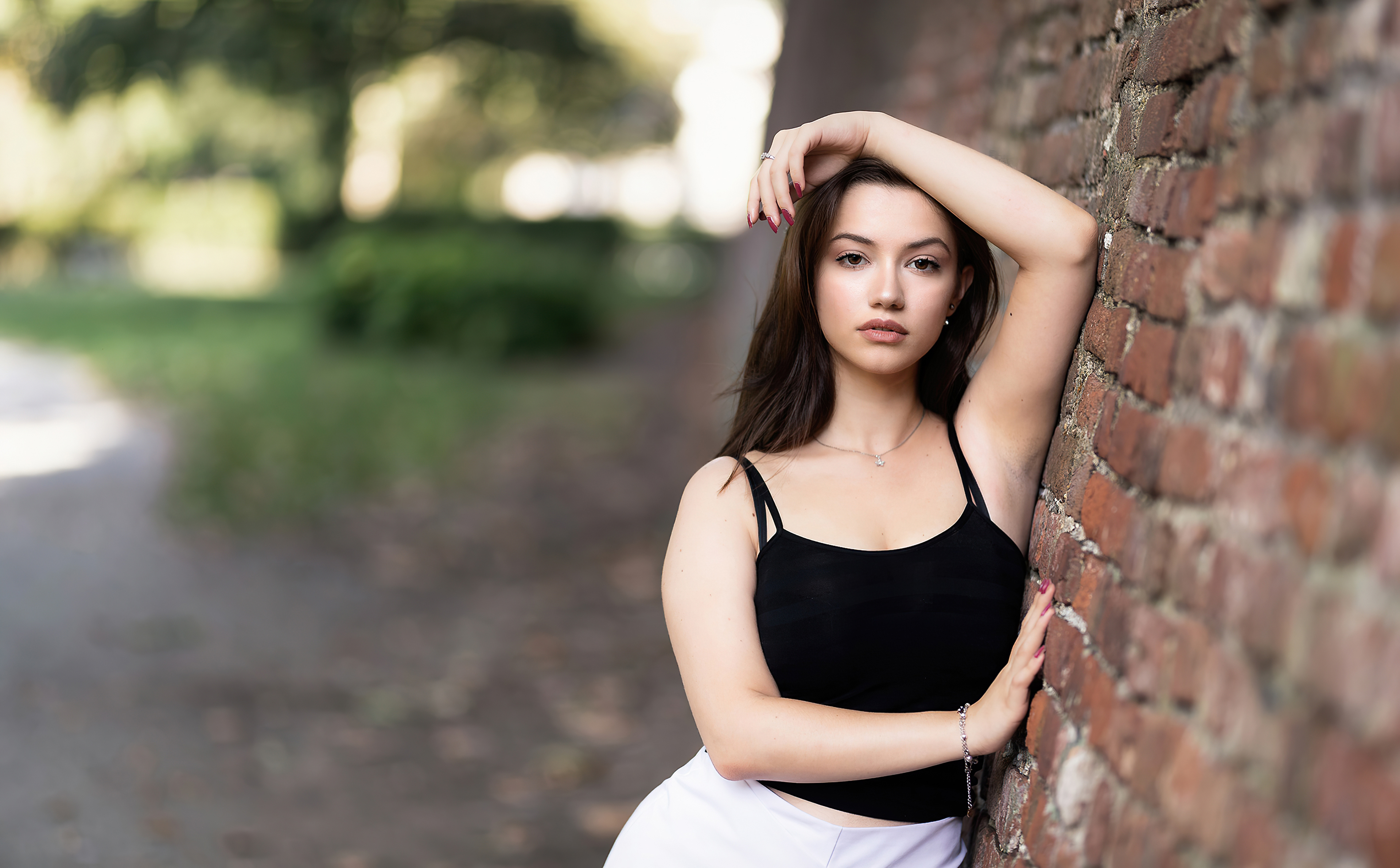 Young woman in black tank top leaning against brick wall HD Wallpaper