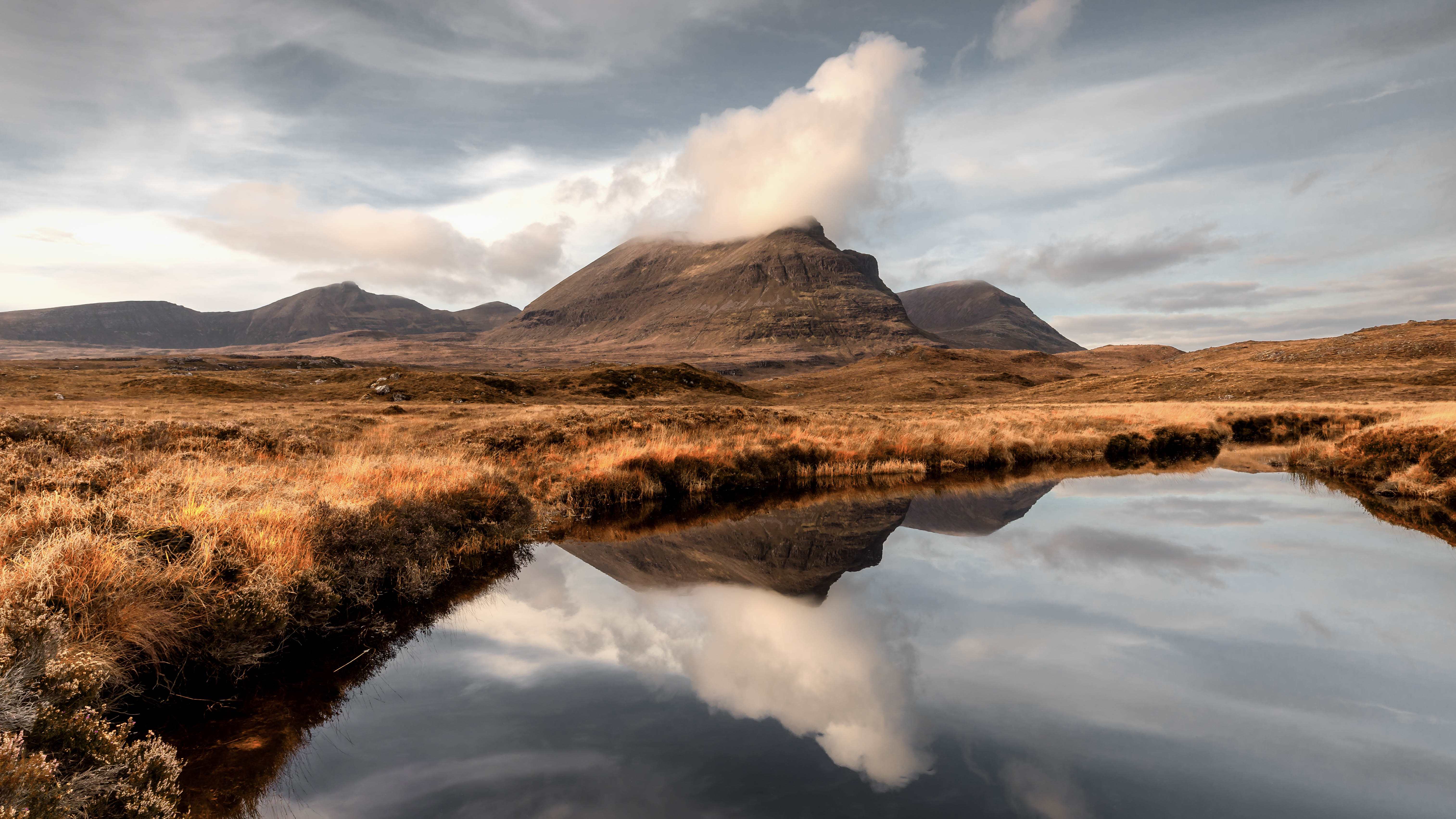 Mountains reflected in a calm lake under a cloudy sky HD Wallpaper
