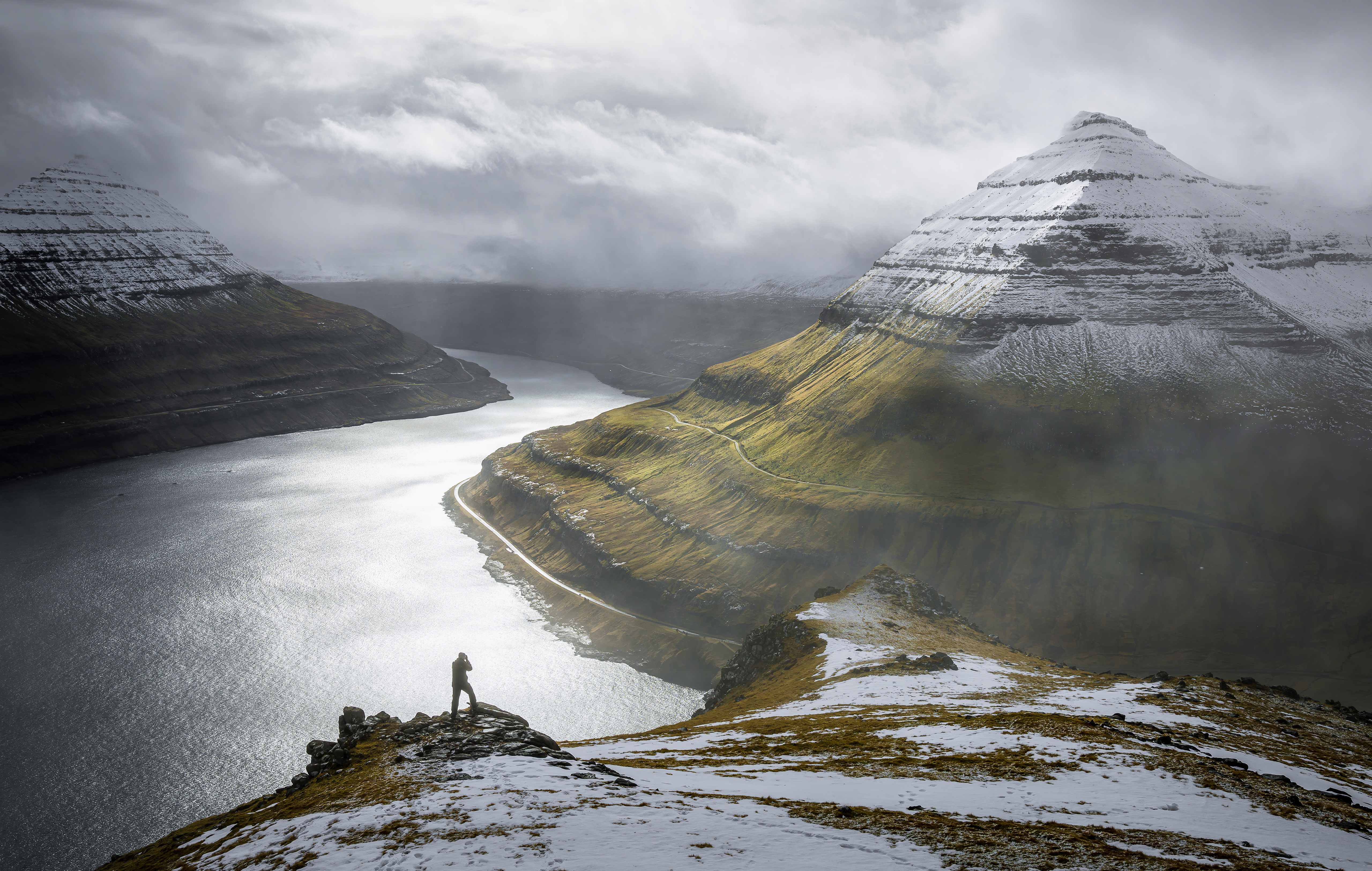 Man on cliff overlooking fjord and mountains HD Wallpaper