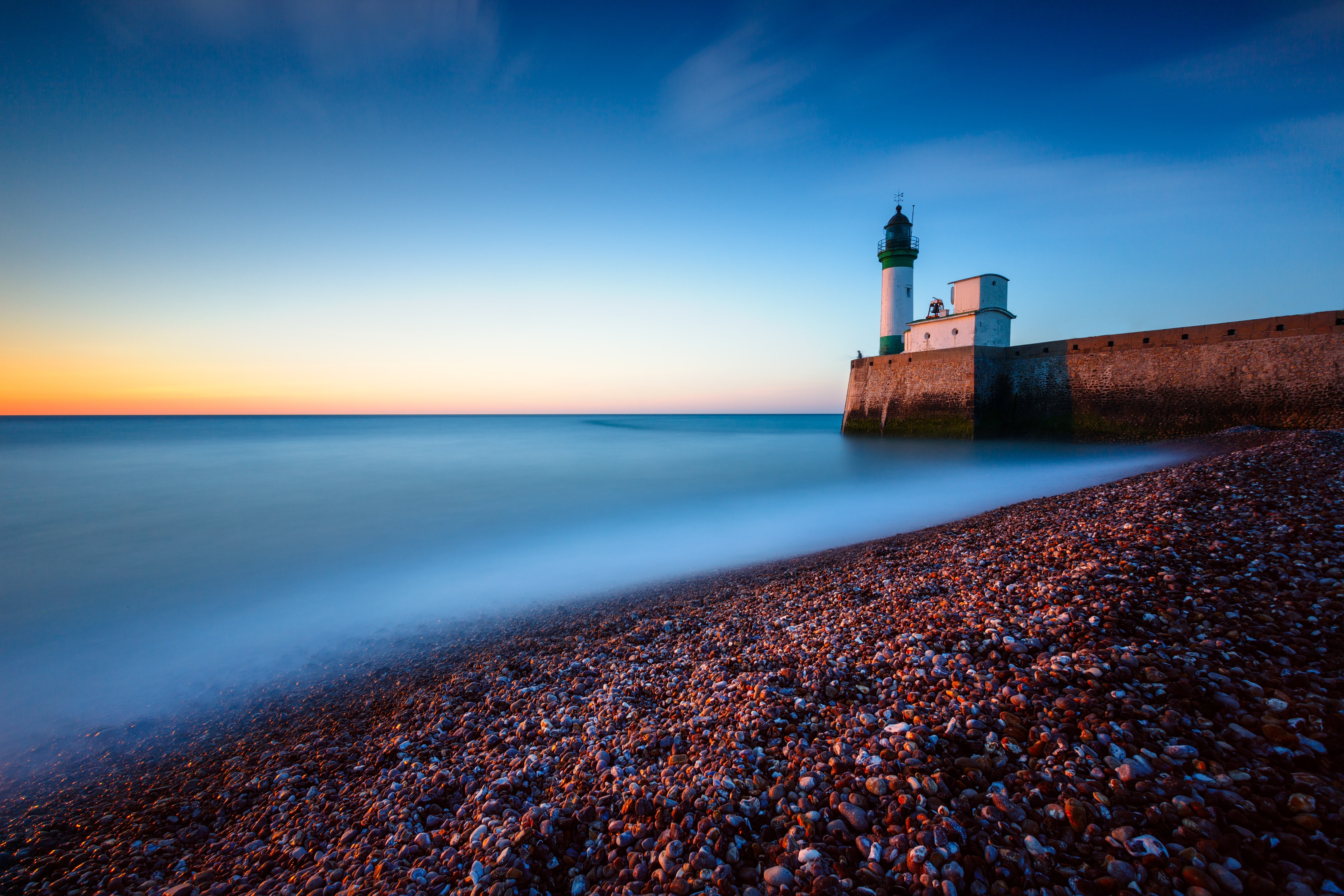 Lighthouse on a stone pier at sunset HD Wallpaper